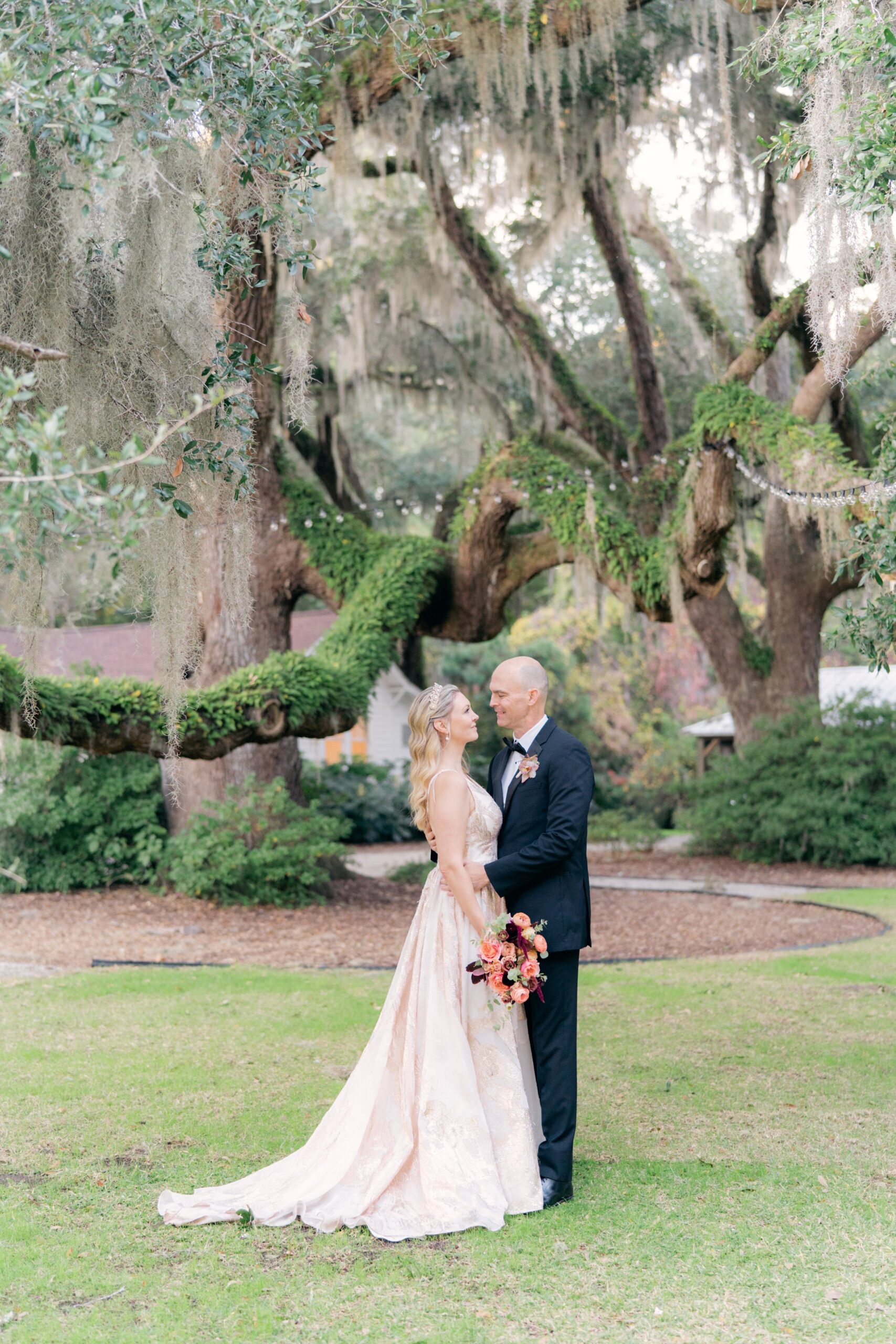 metallic pink wedding dress. groom in black tux. spanish moss and mossy live oak trees
