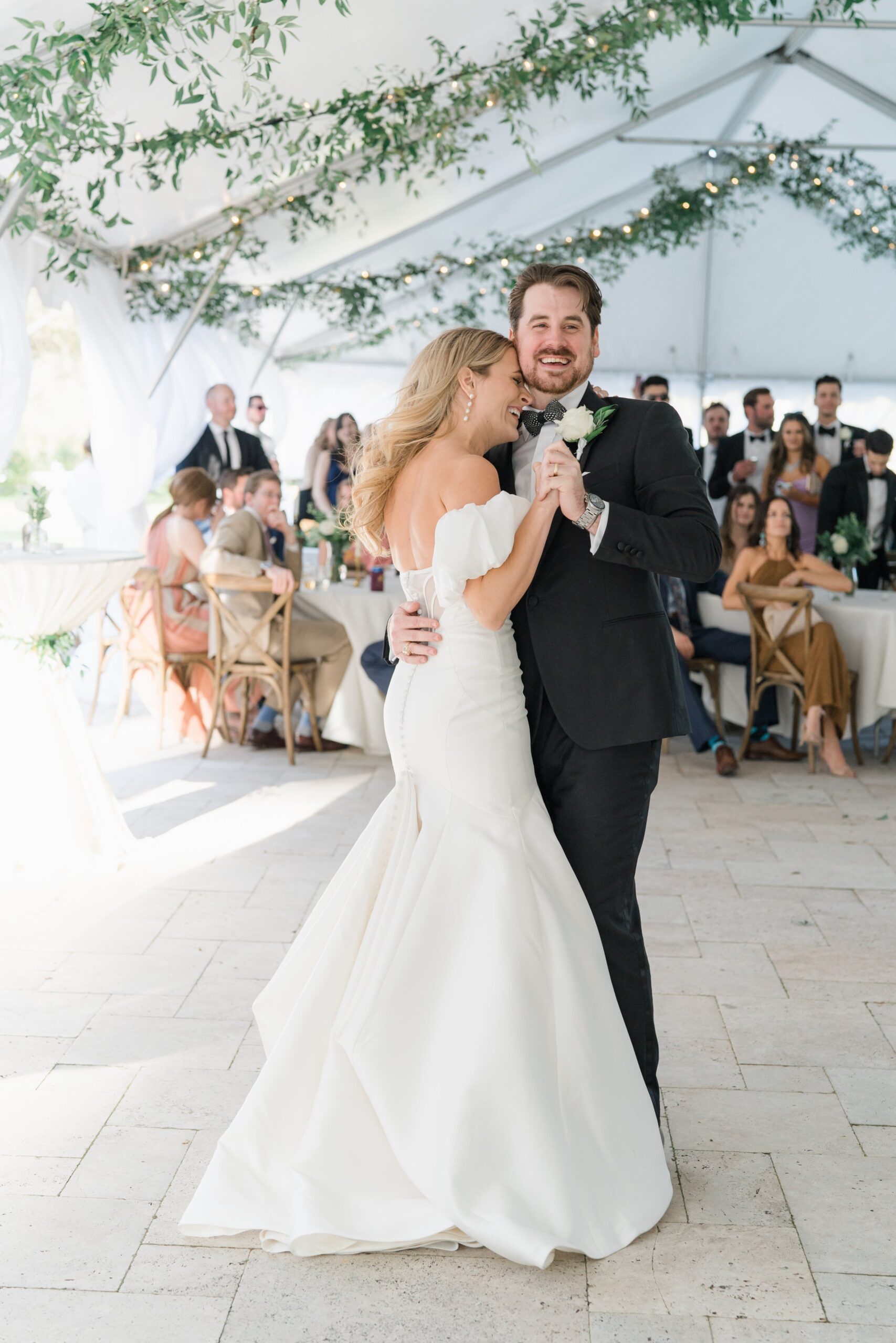 Bride and groom first dance under greenery and string lights. spring charleston wedding