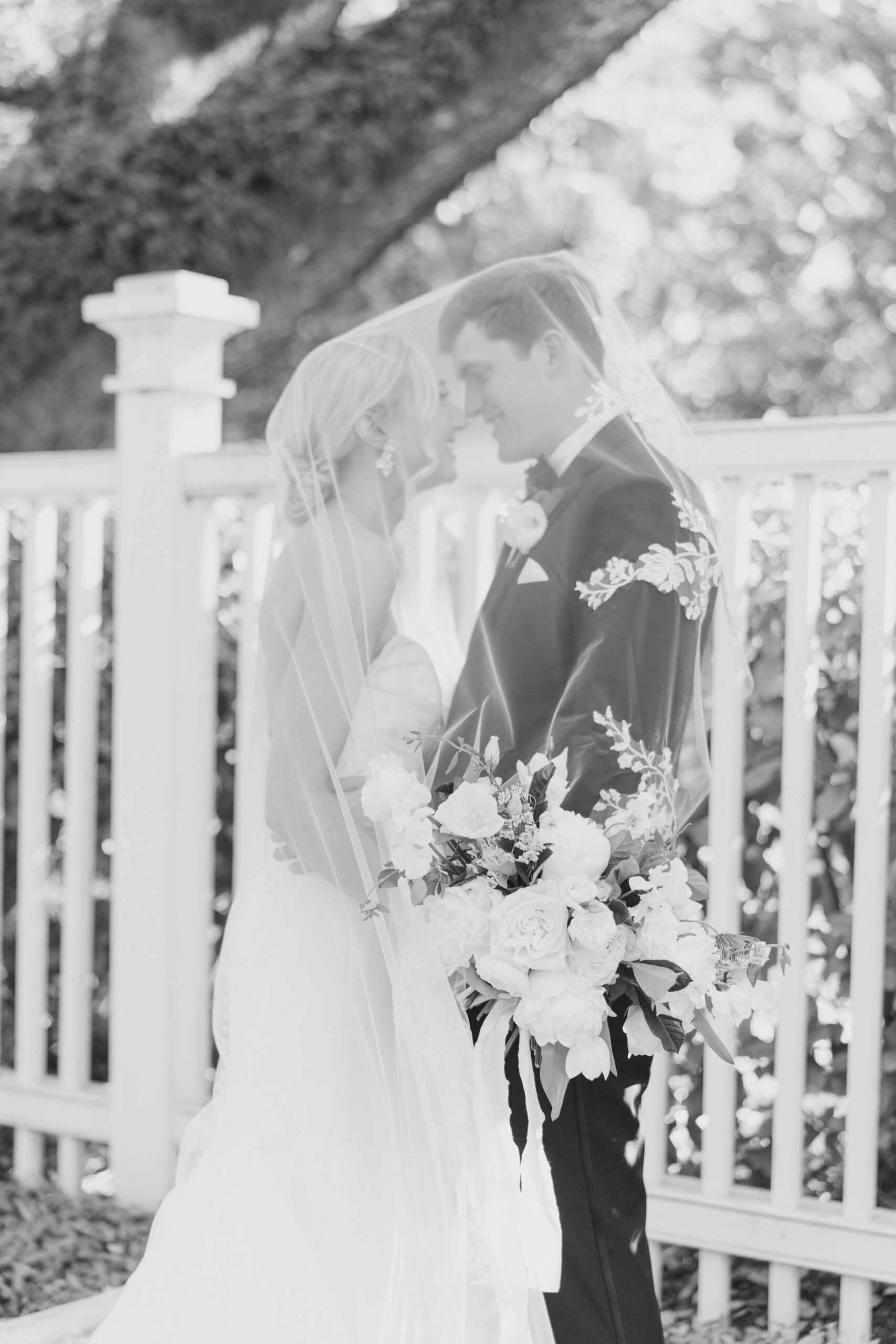 black and white wedding photo. bride and groom covered in flower detailed veil.