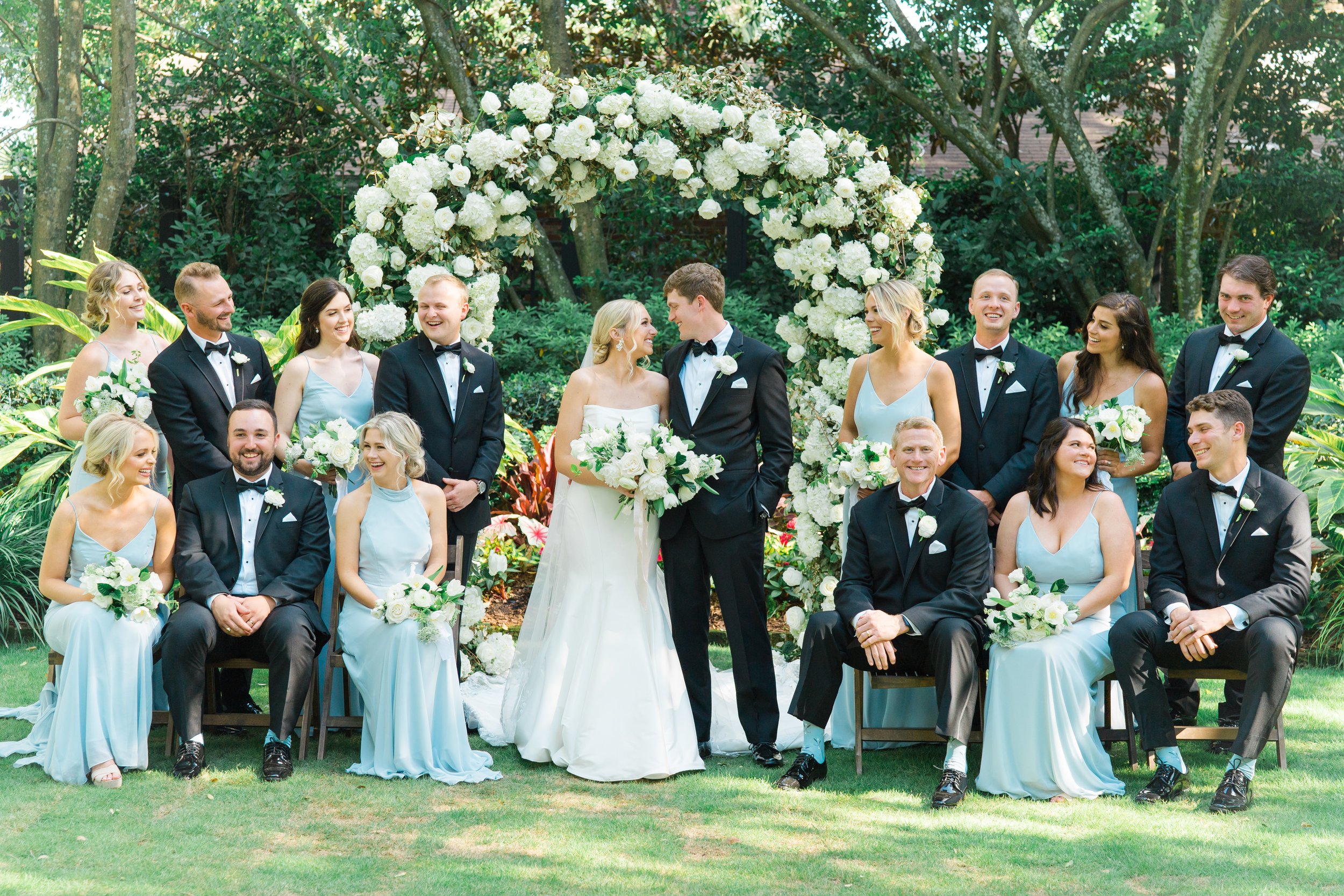 Full bridal party formal picture wit seating. ten foot tall floral arch at wedding ceremony site.