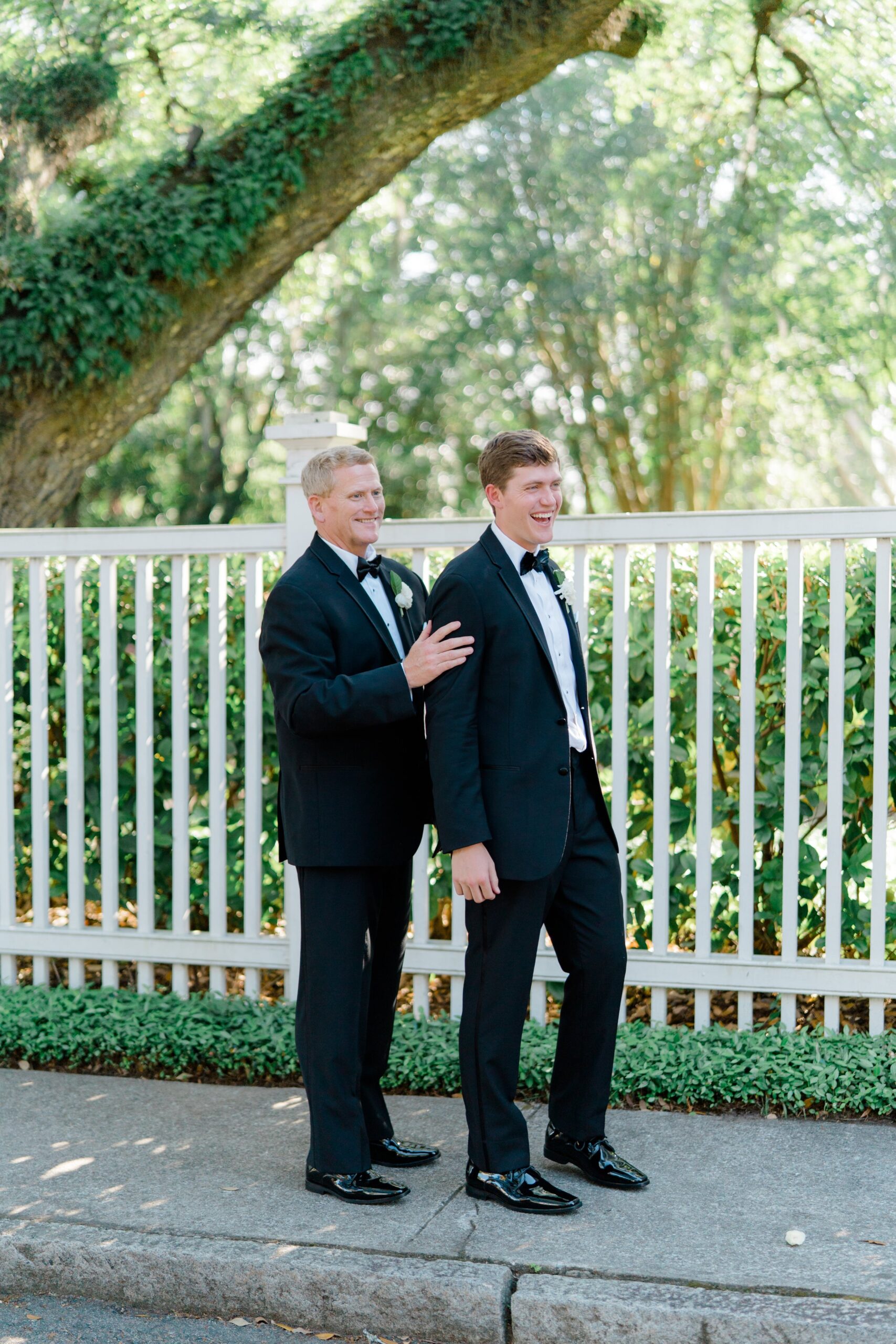 Groom with his dad at Governor Thomas Bennett house wedding. Standing on sidewalk with live oak and greenery.