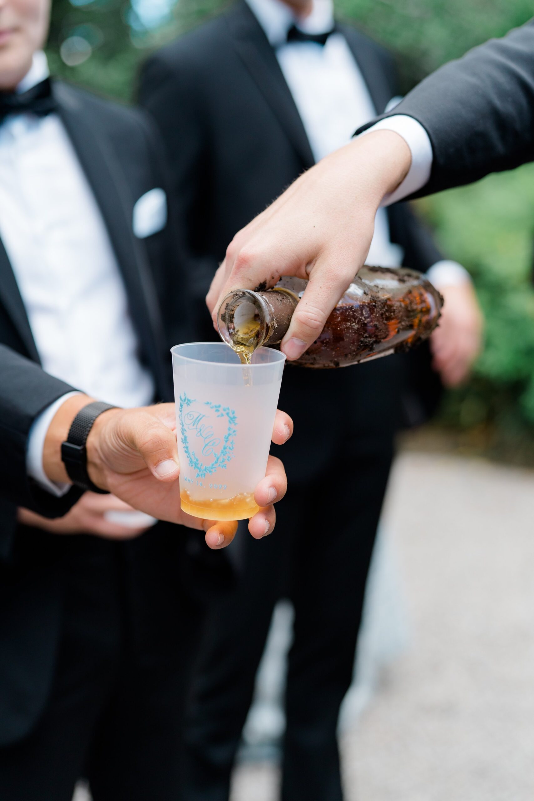 Groom pours bourbon into custom wedding cups with light blue custom insignia