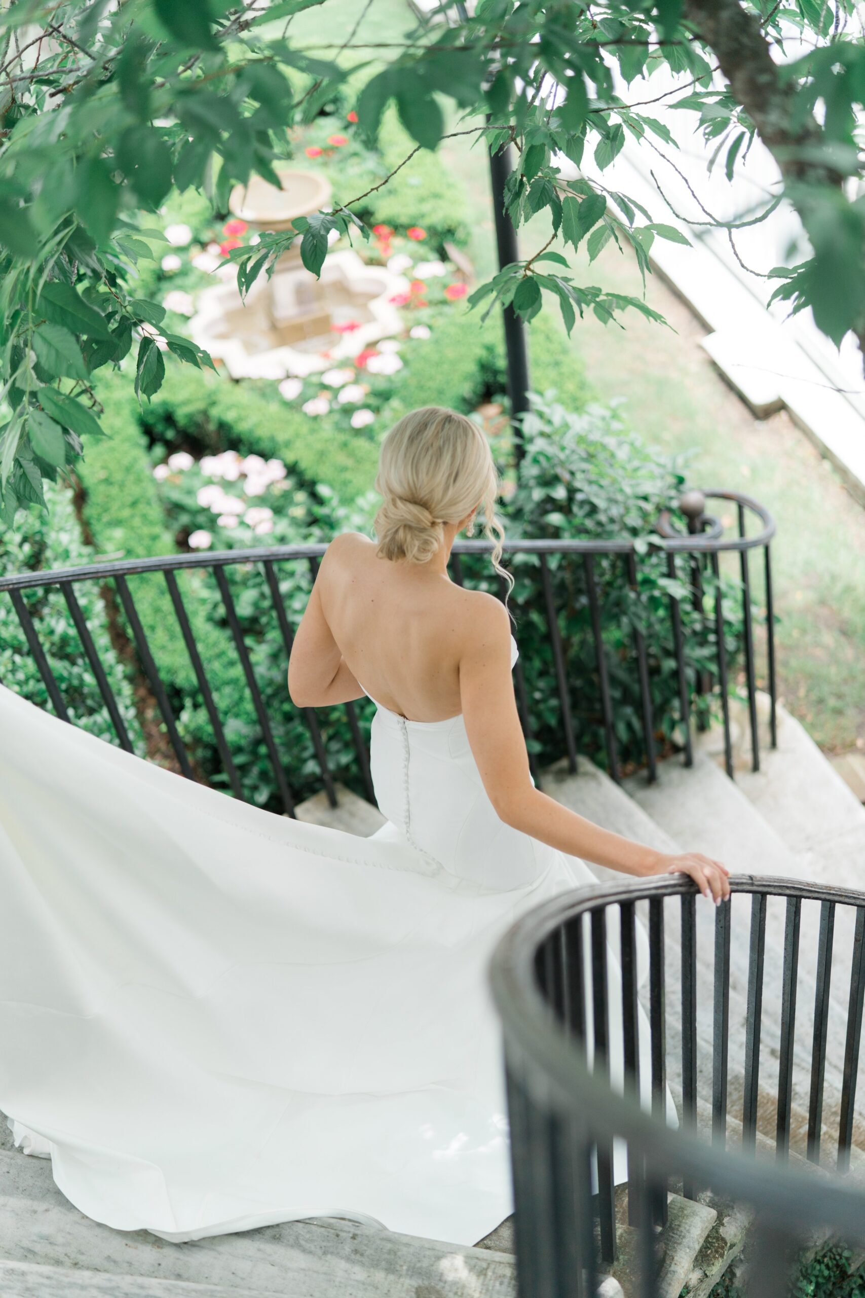 Bride descends stairs at Charleston spring wedding with fountain and garden with greenery.