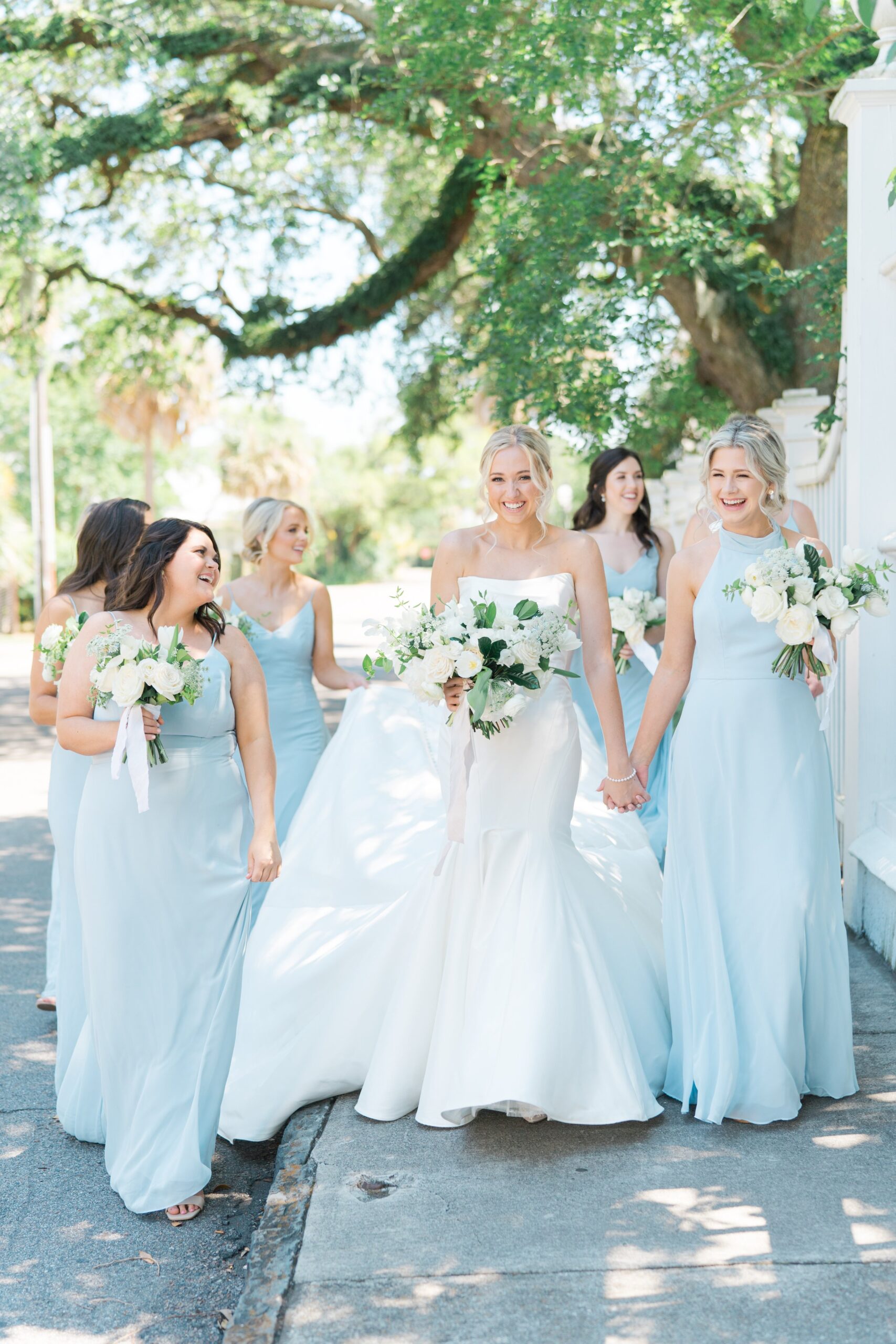 Bride walking with bridesmaids and holding hand of maid of honor. Downtown Charleston weddings. Bridesmaids in light blue dresses.