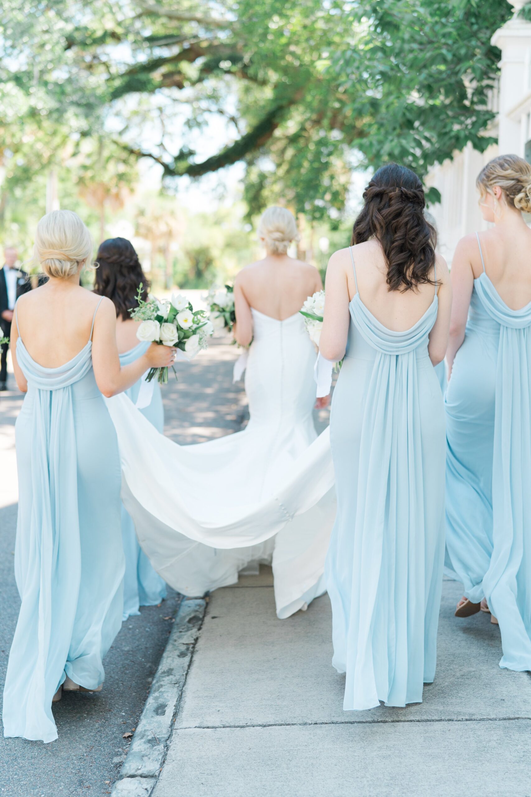 Bride and bridesmaids walking away. Bridesmaid dresses with flowy details on back of dress.