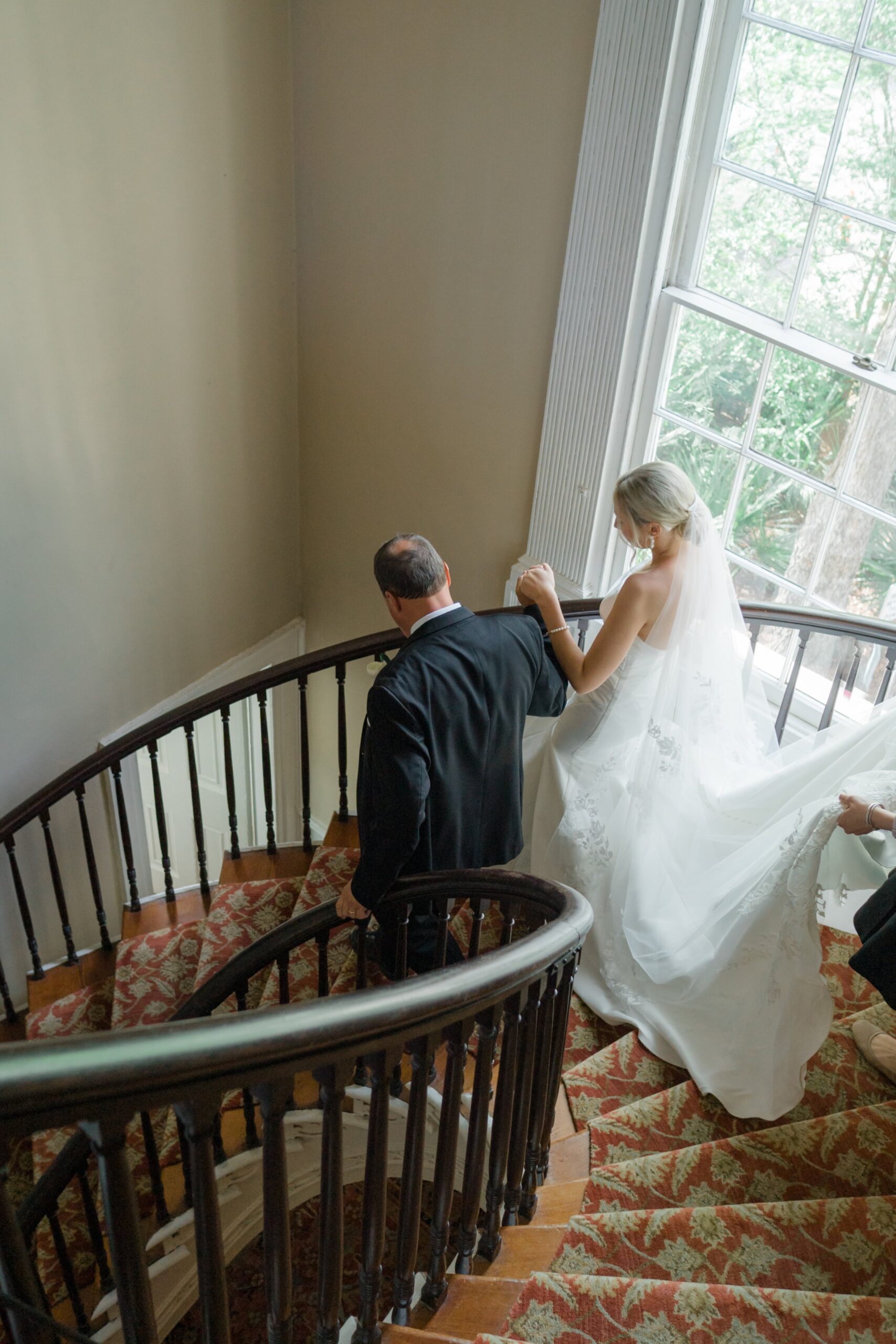 Bride walks down curved stairway with father before spring wedding ceremony. Charleston wedding.