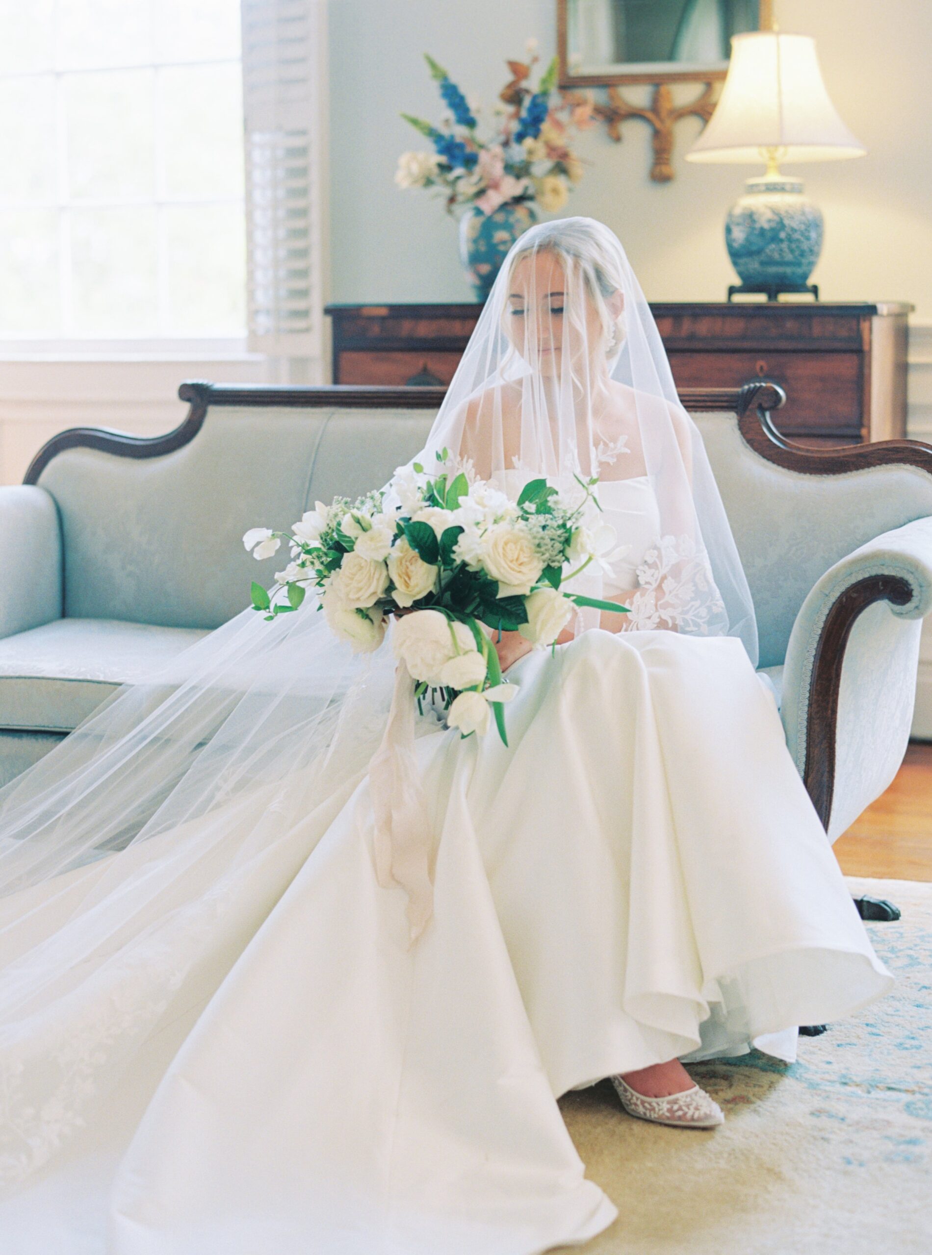 East Coast Wedding Photographer. Charleston film photographer. Veil-covered bride sitting on light blue couch.