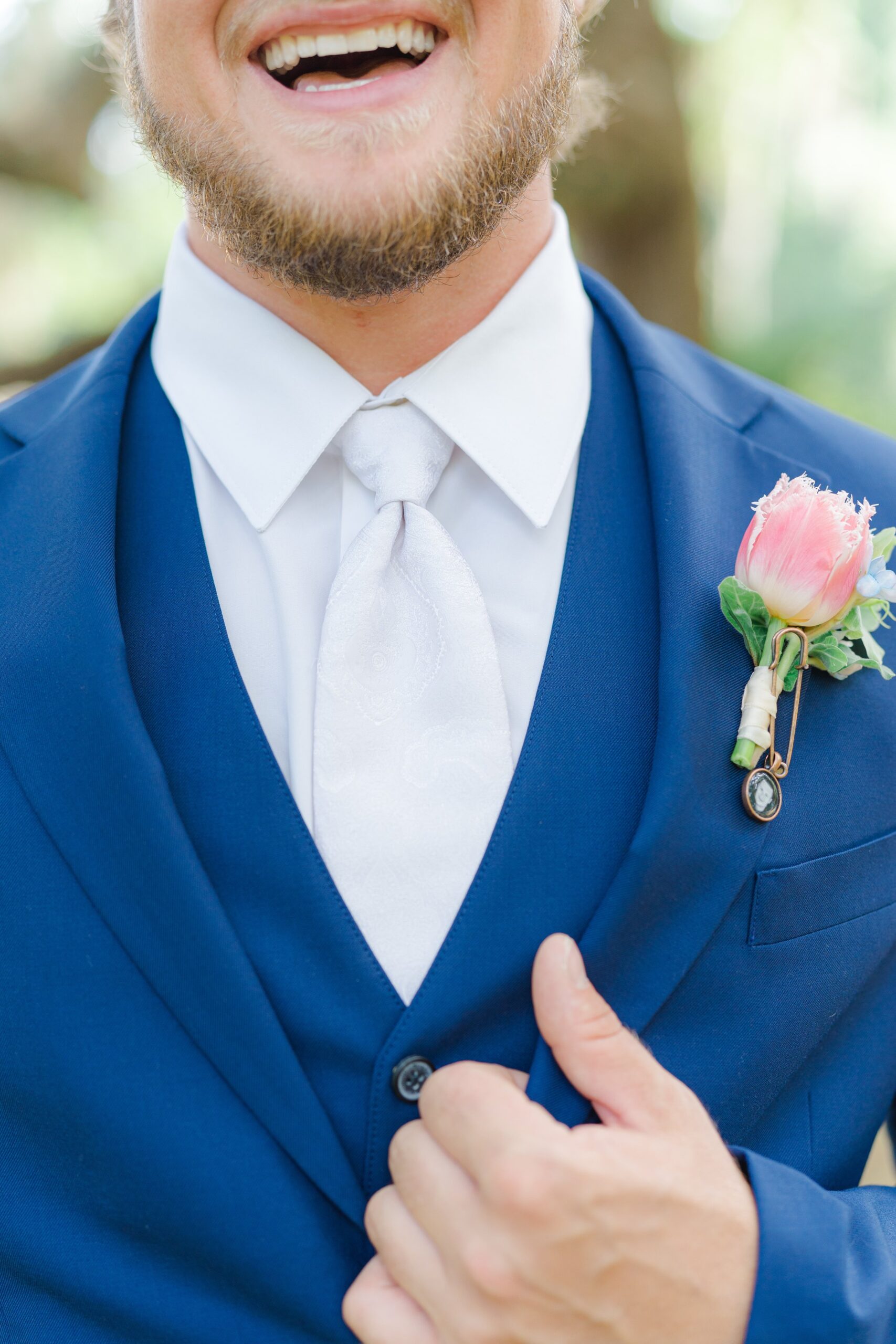 smiling groom in blue suit, white tie, and pink boutonniere