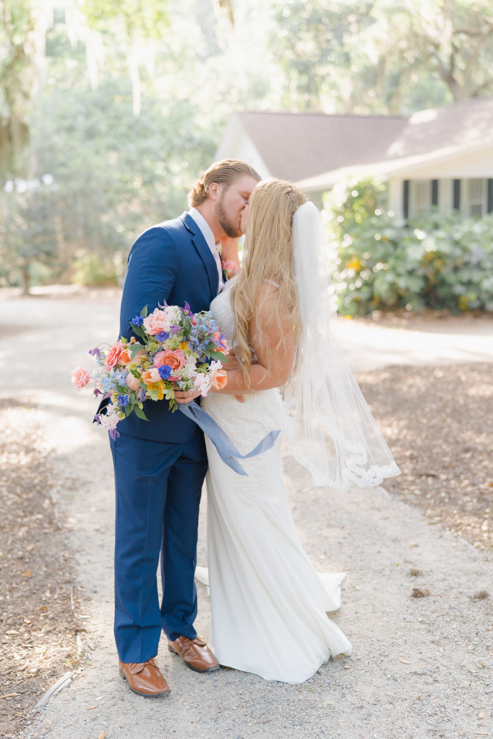bride and groom kiss with sunlight and wildflower wedding bouquet