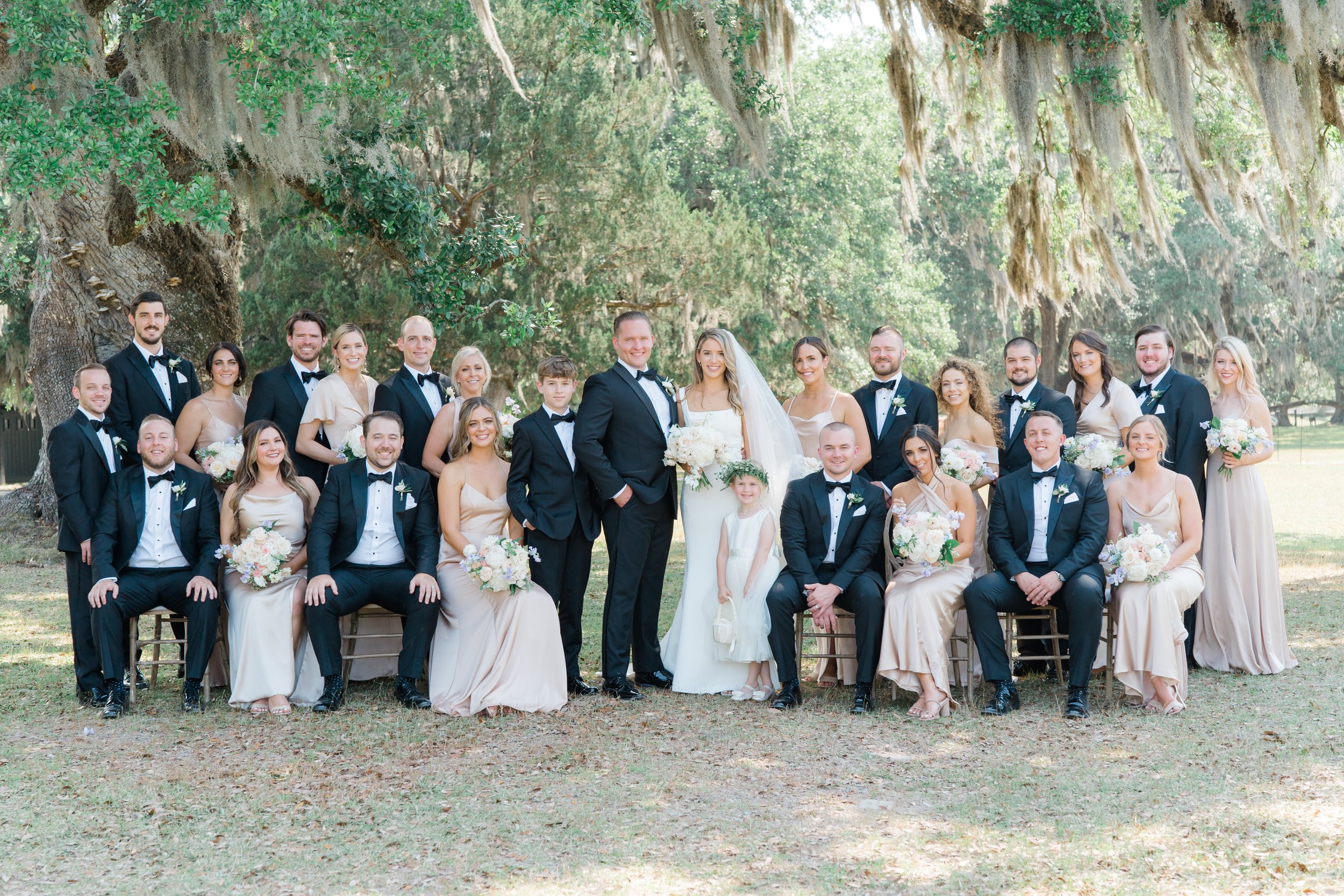 Full bridal party group photo. Black tuxedo groomsmen. Champagne colored bridesmaid dresses.