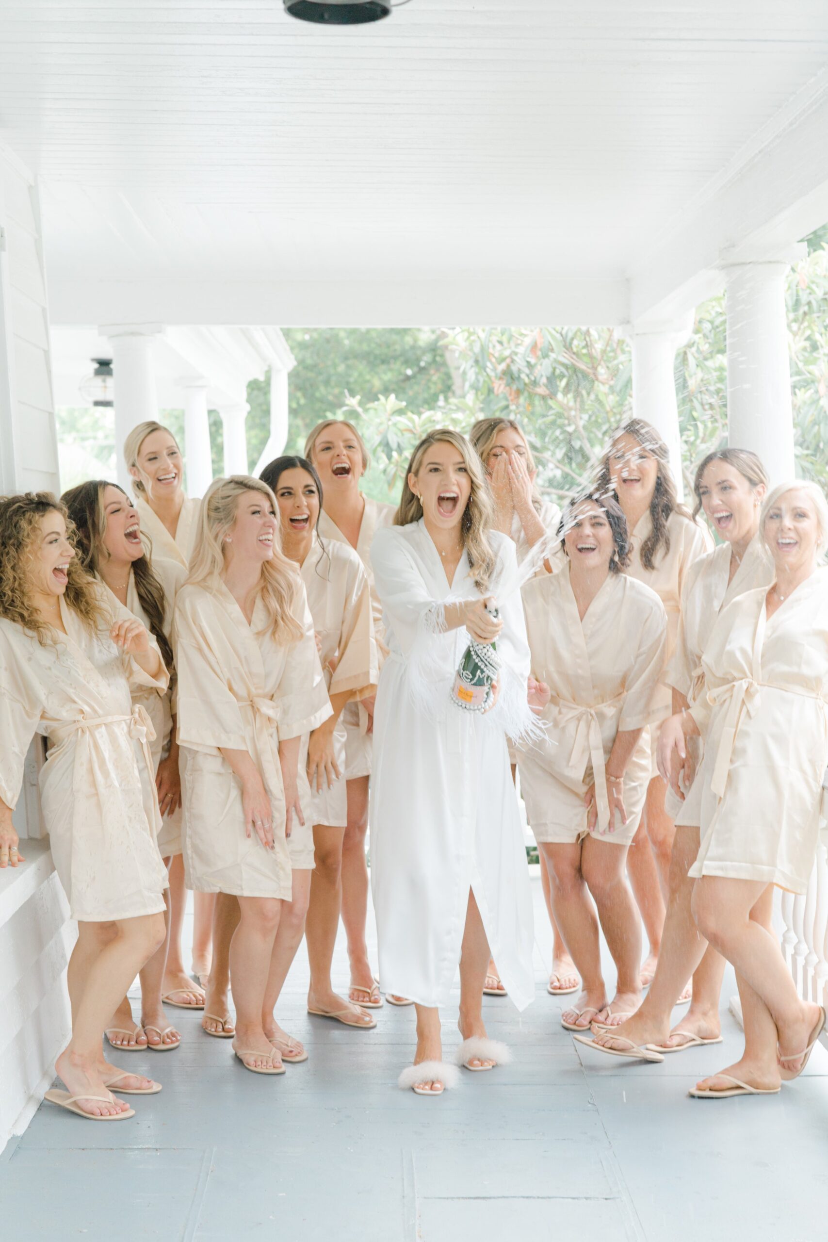 Bride and bridesmaids in getting ready robes spraying champagne on downtown Charleston porch