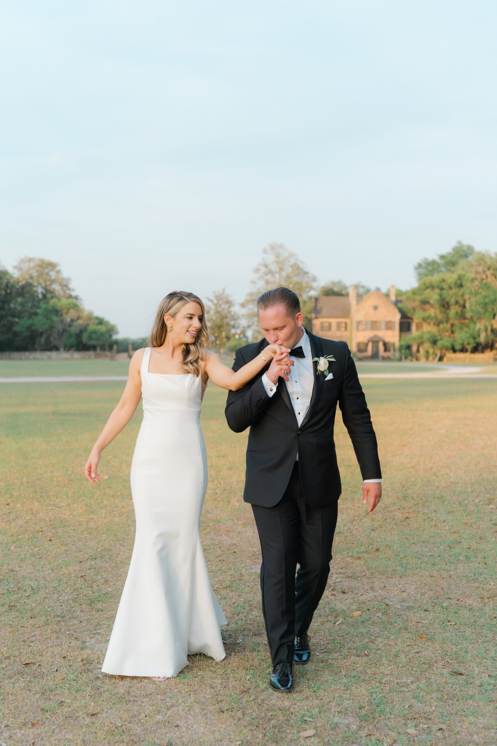 Middleton Place spring bride and groom walking in field. Groom kissing brides hand while walking.