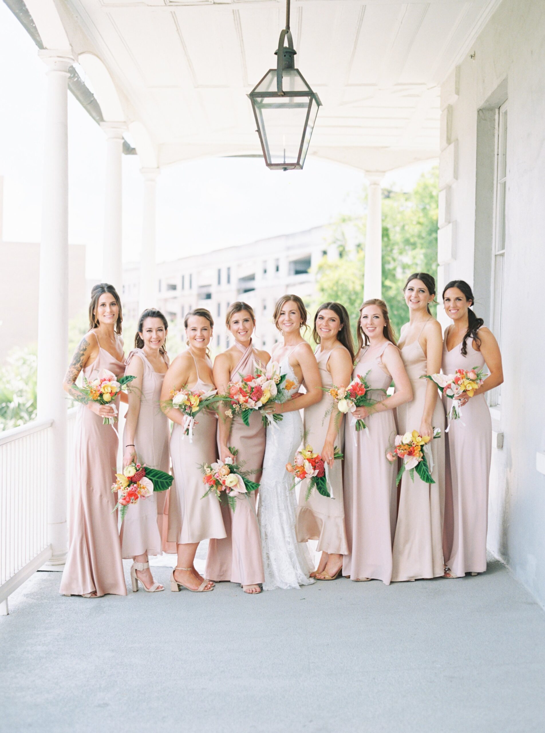 Bride and bridesmaids group photo. Bridesmaids in neutral tone with bright tropical flowers. Charleston spring wedding.