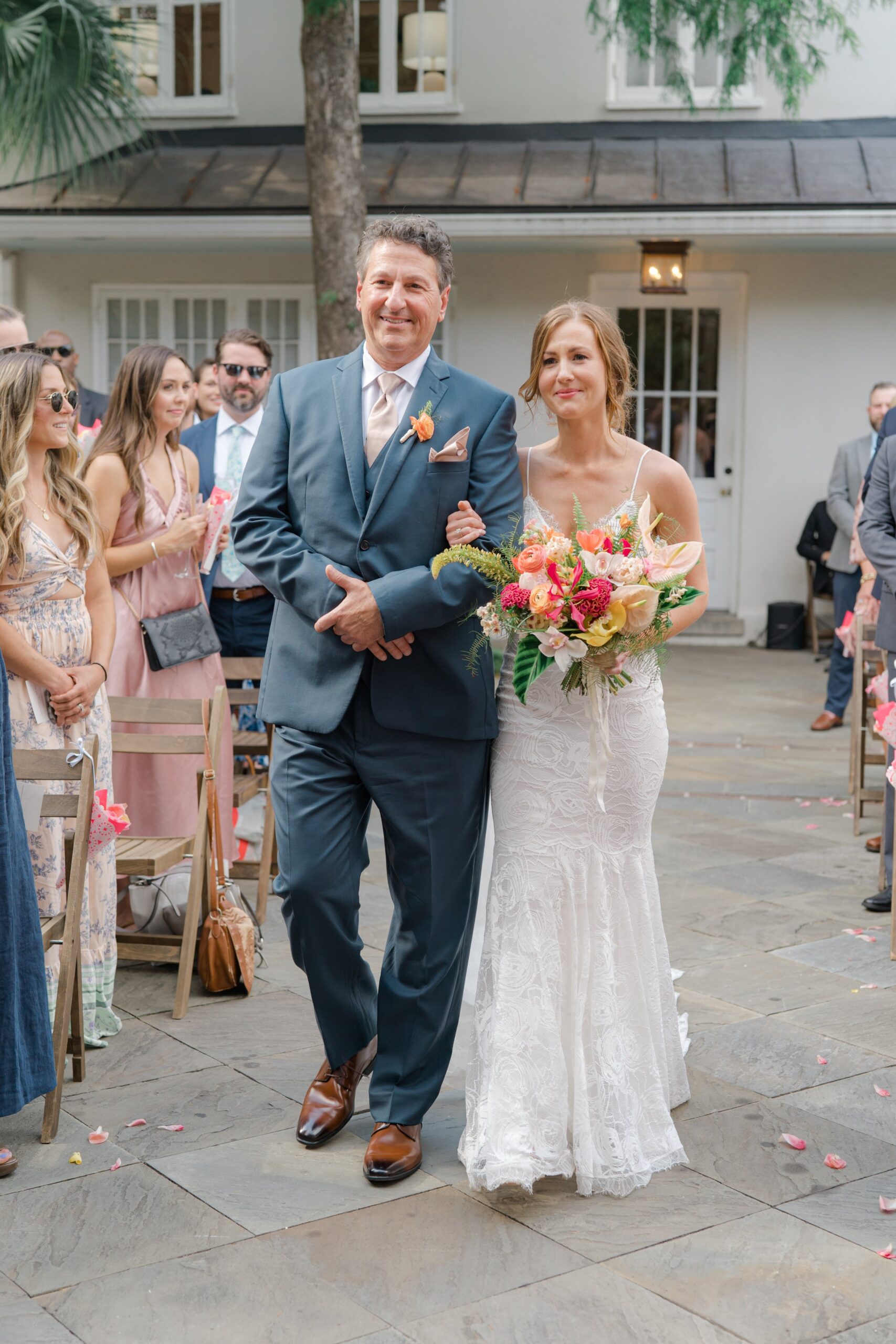 Emotional bride with tropical flowers walks to groom at outdoor wedding ceremony in Charleston.