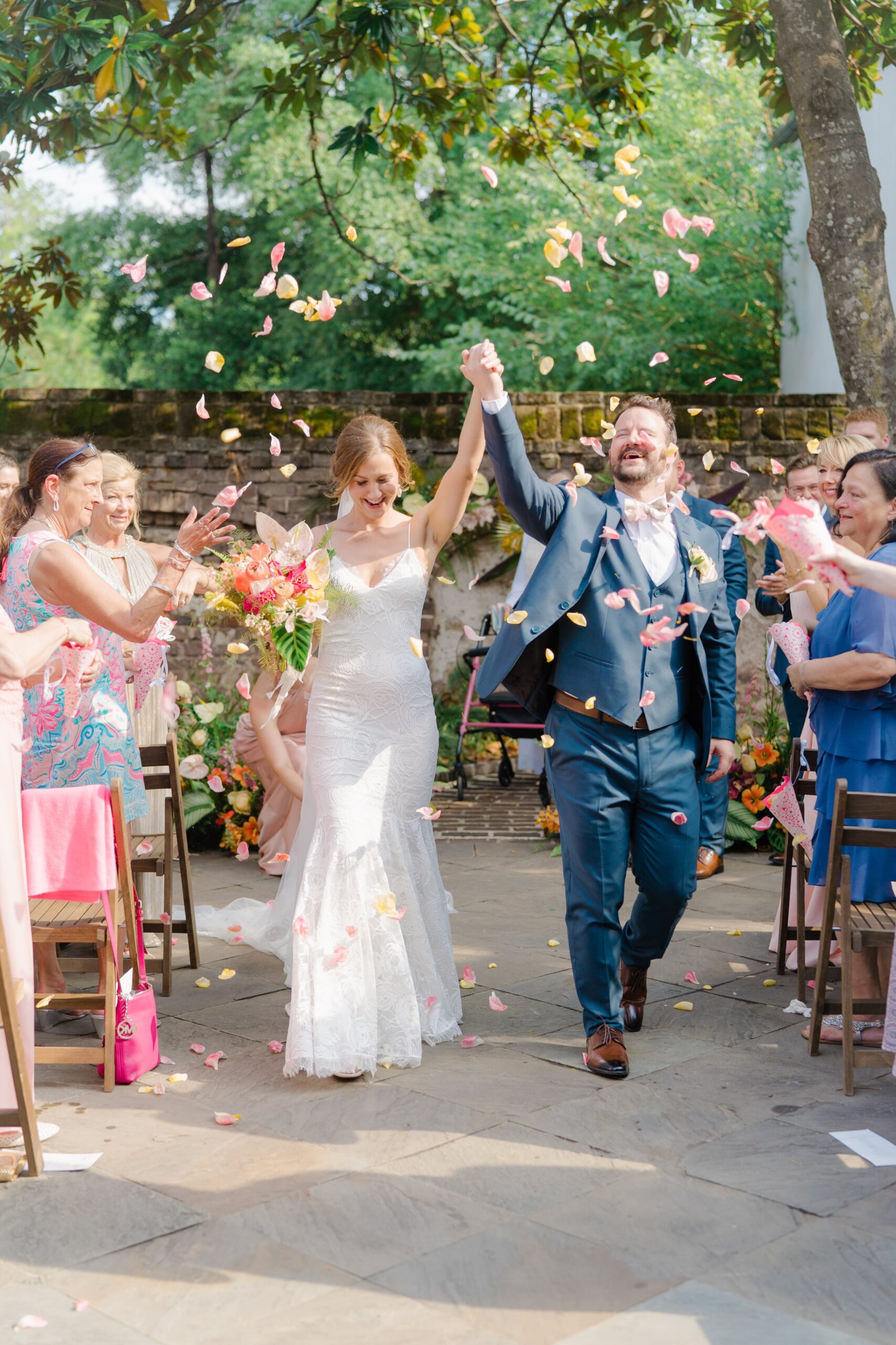 Pink petal toss outdoor wedding ceremony exit. Elated bride and groom walk down the aisle.