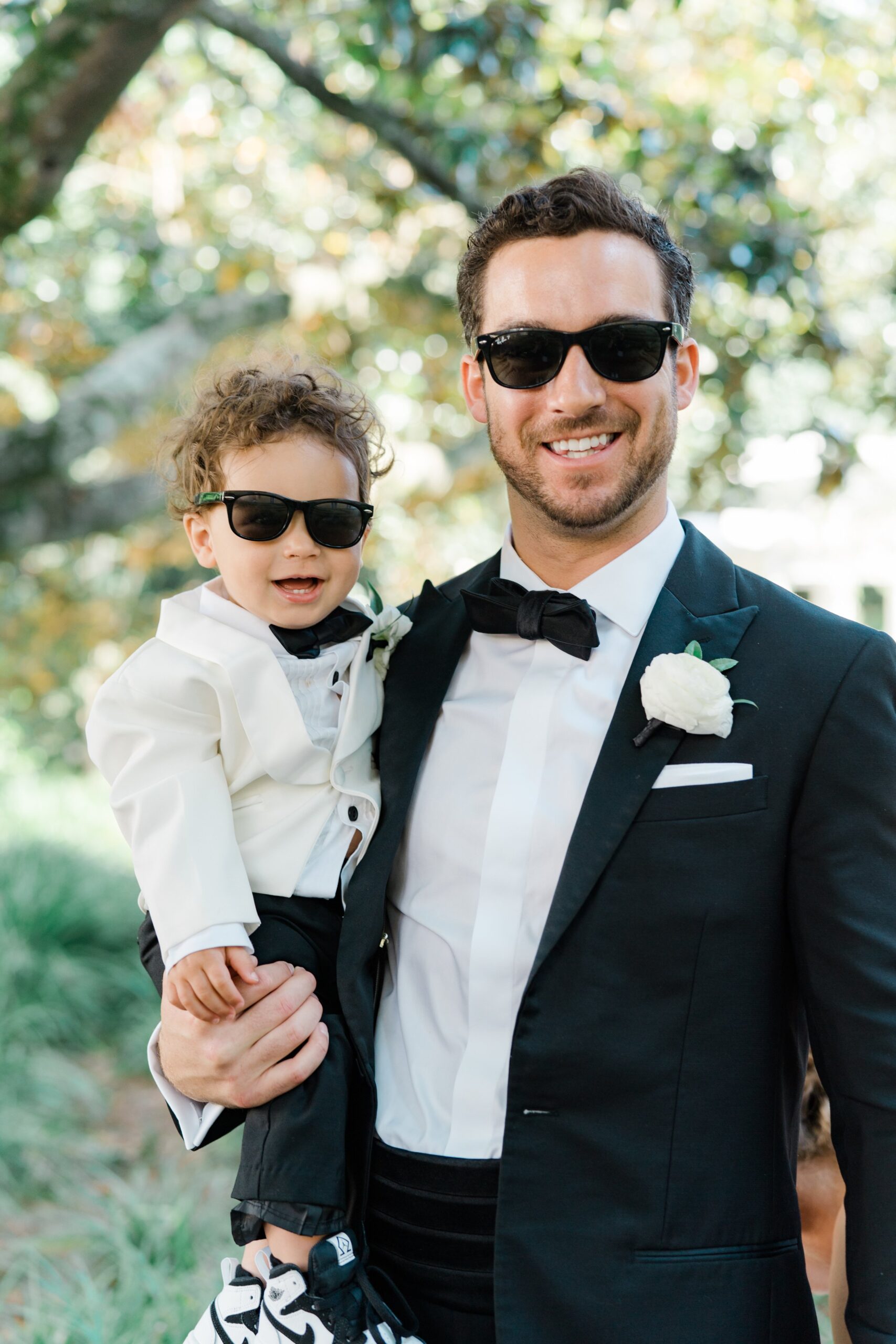 Father and son wearing tuxedos and sunglasses.