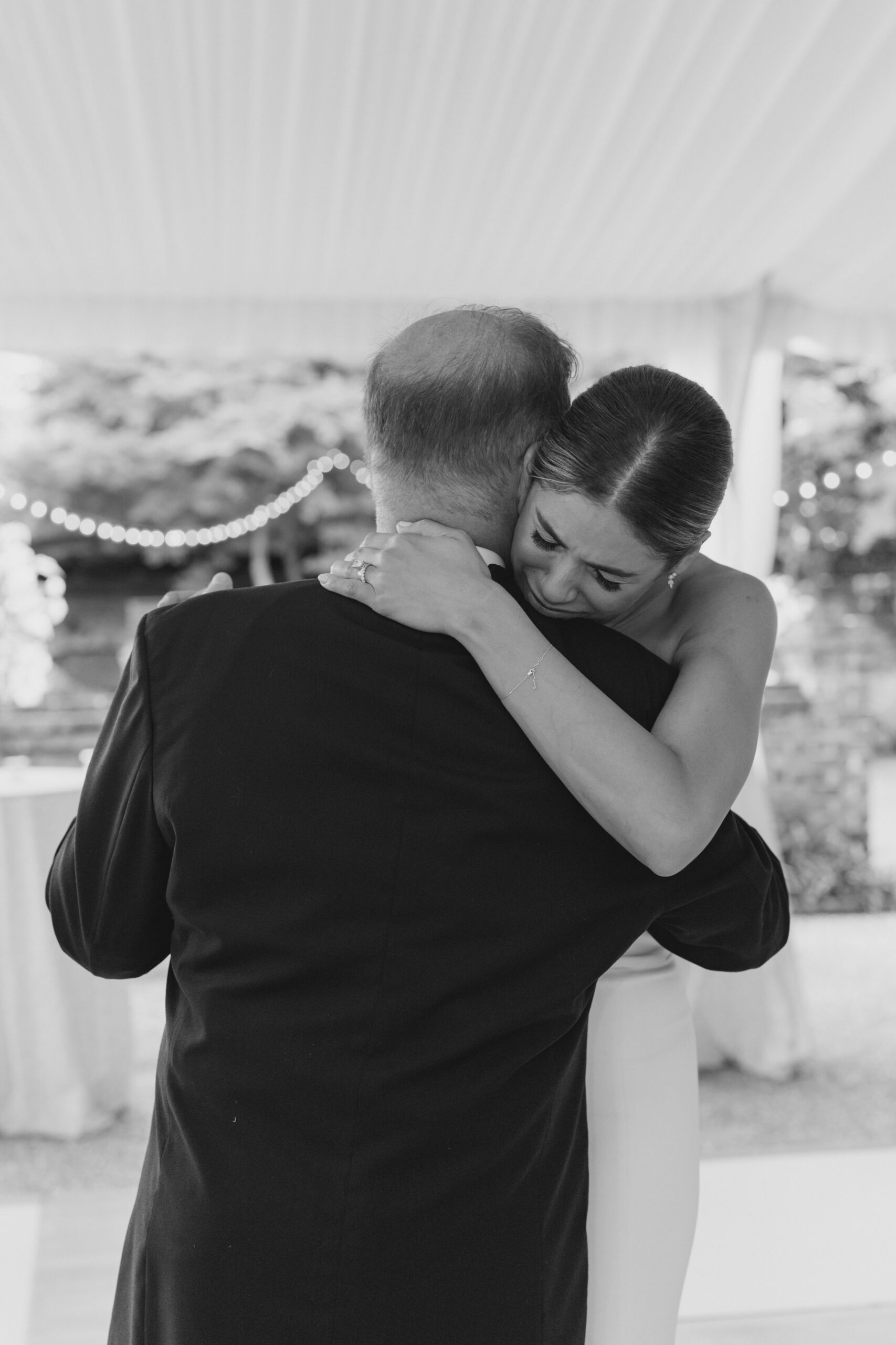 emotional bride hugs dad during wedding. black and white wedding photo.