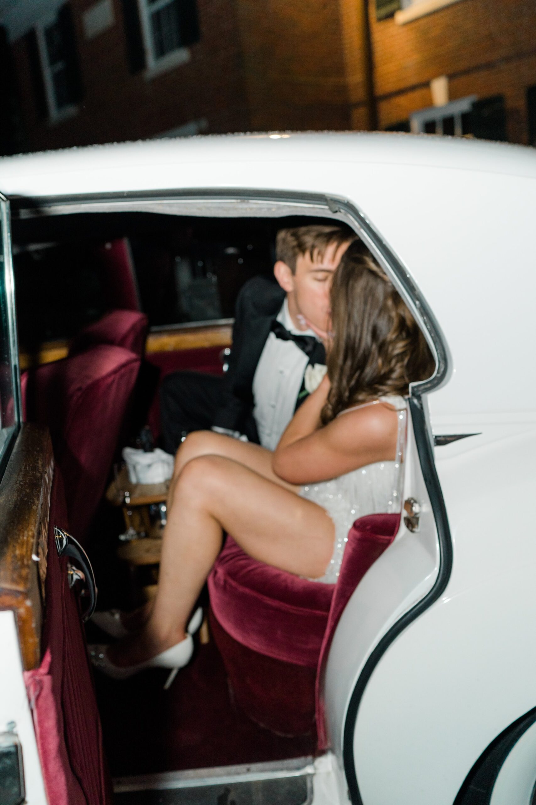 bride and groom kiss in the back seat of vintage getaway car.
