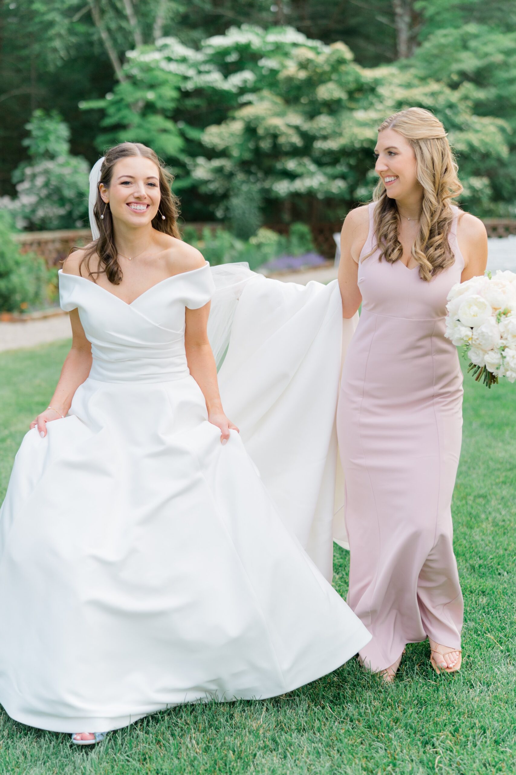 Maid of honor in dusty pink dress helping sister walk with large wedding dress.