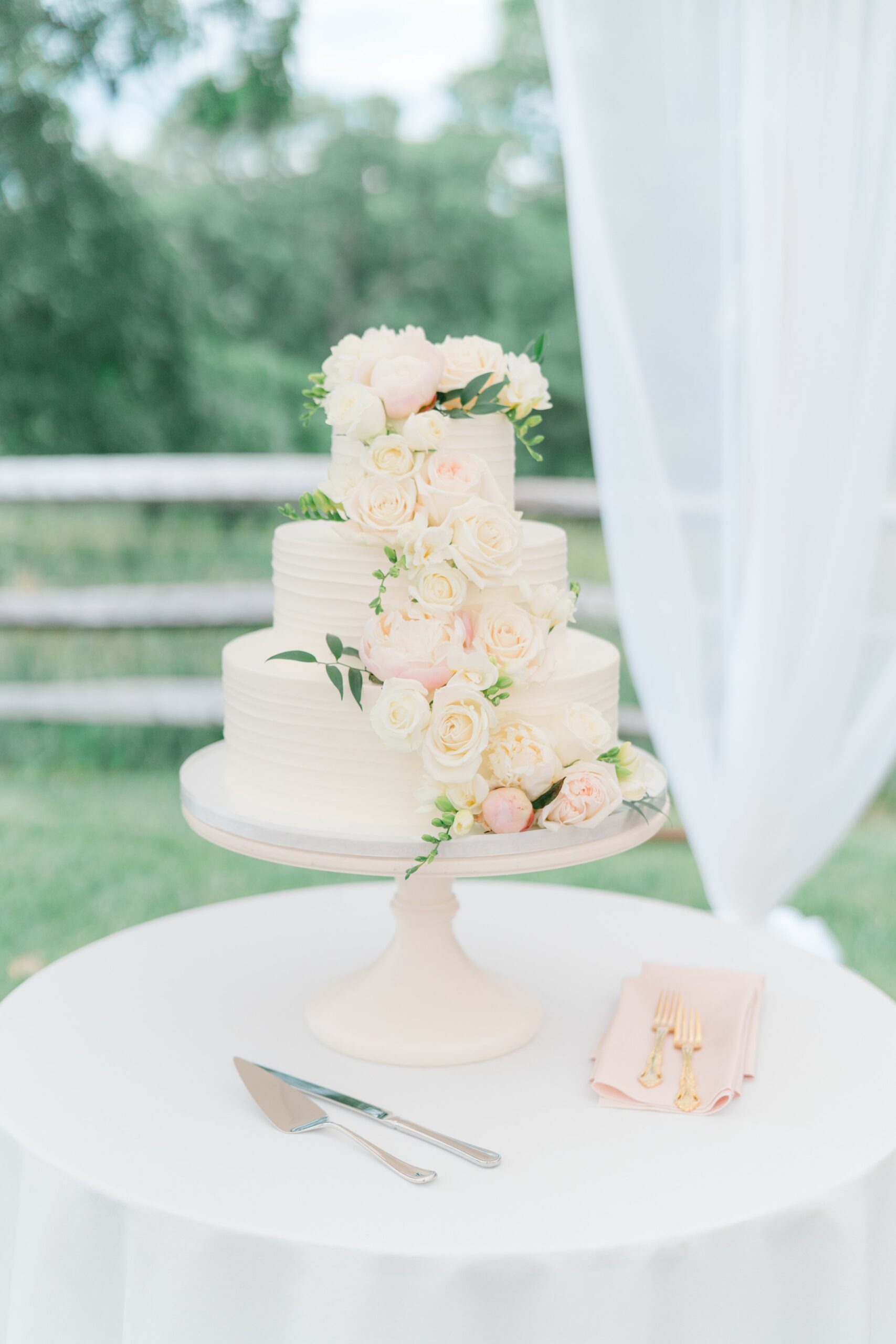 three tiered white wedding cake with white and pale pink flowers flowing down the front and touches of greenery. Boston summer wedding.
