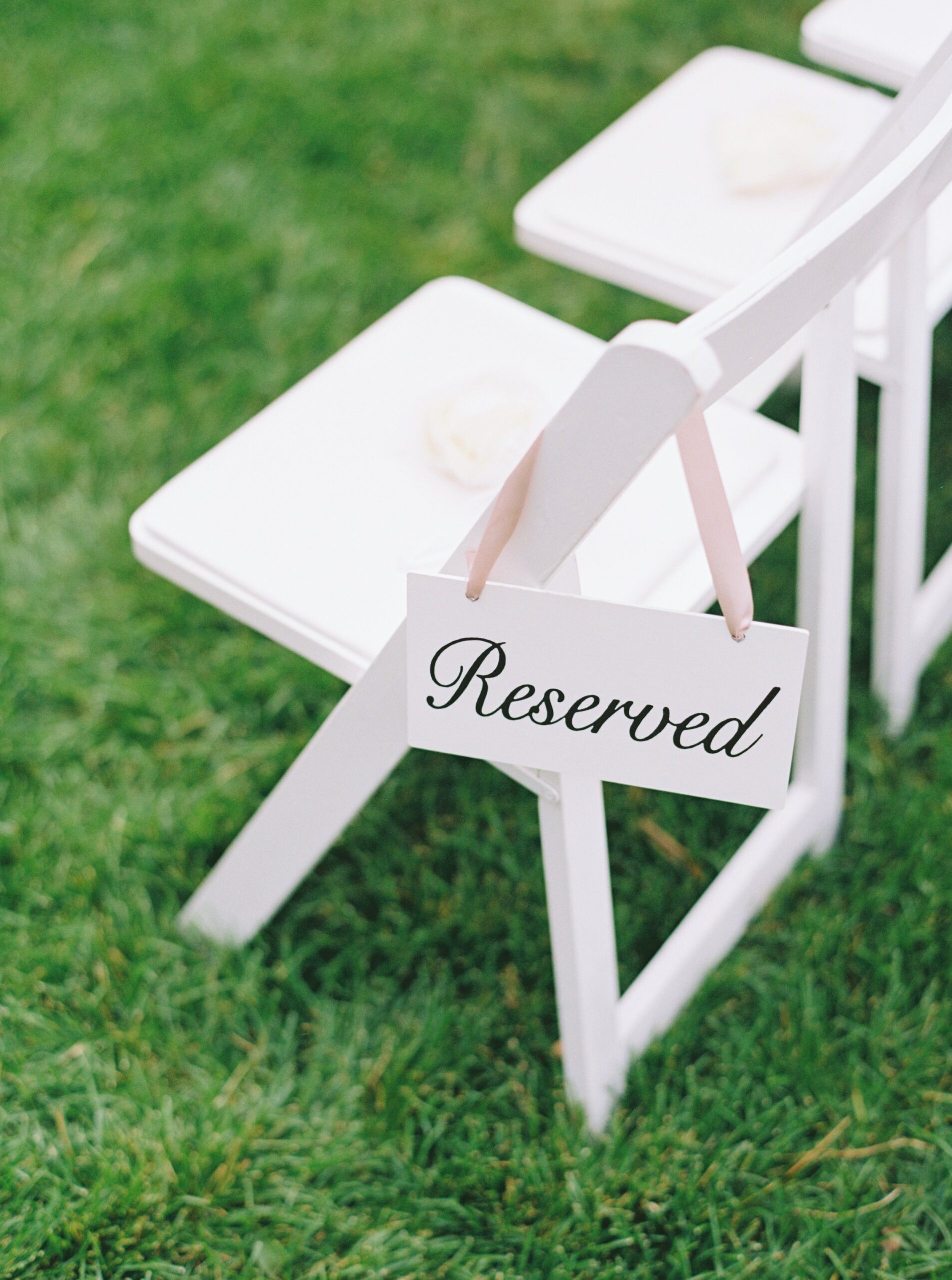 Elegant reserved sign with pink ribbon on white chair