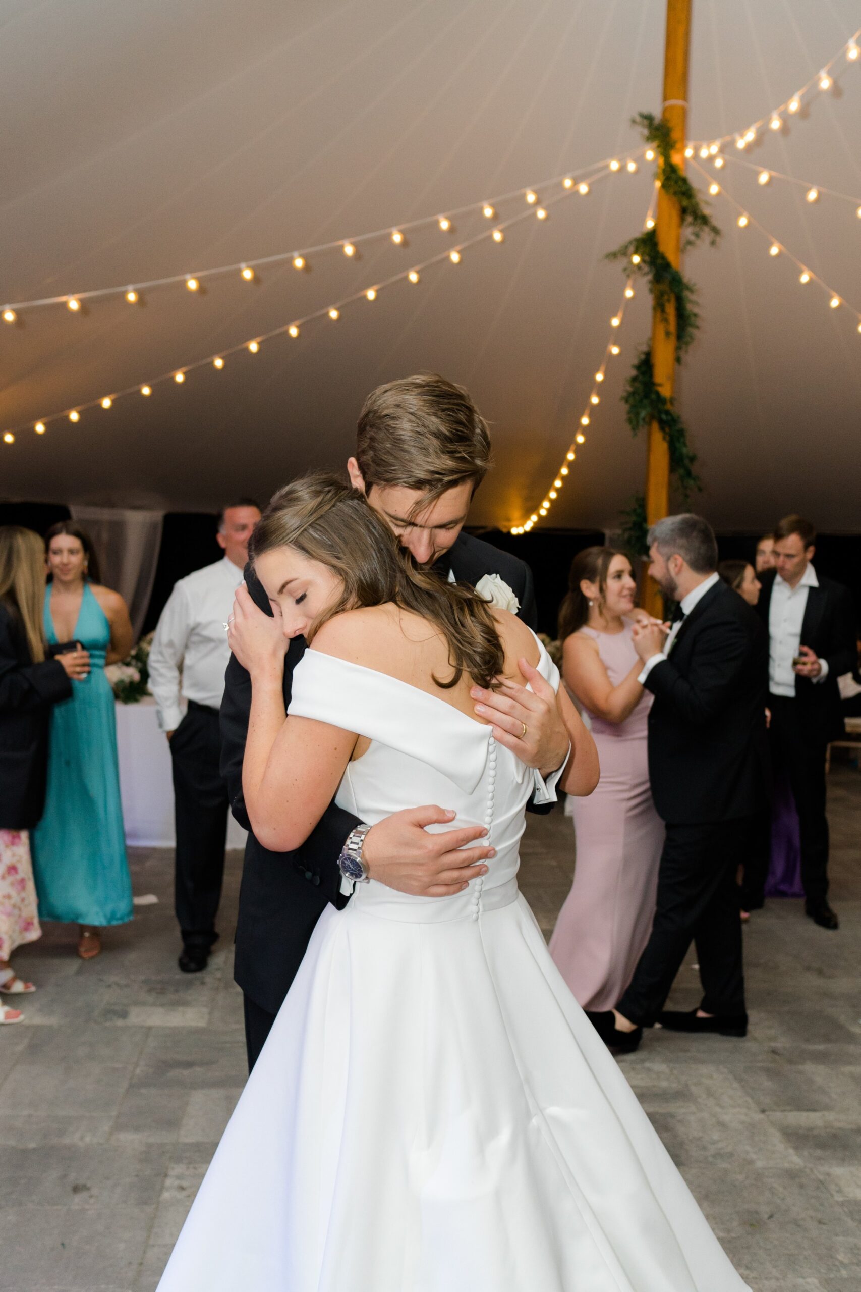 emotional bride and groom share sweet embrace. String lights in sperry tent during summer wedding.