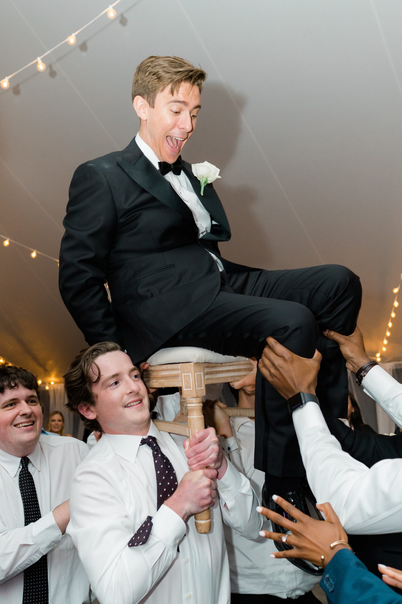 Groom gets picked up in chair during outdoor wedding reception in Boston.