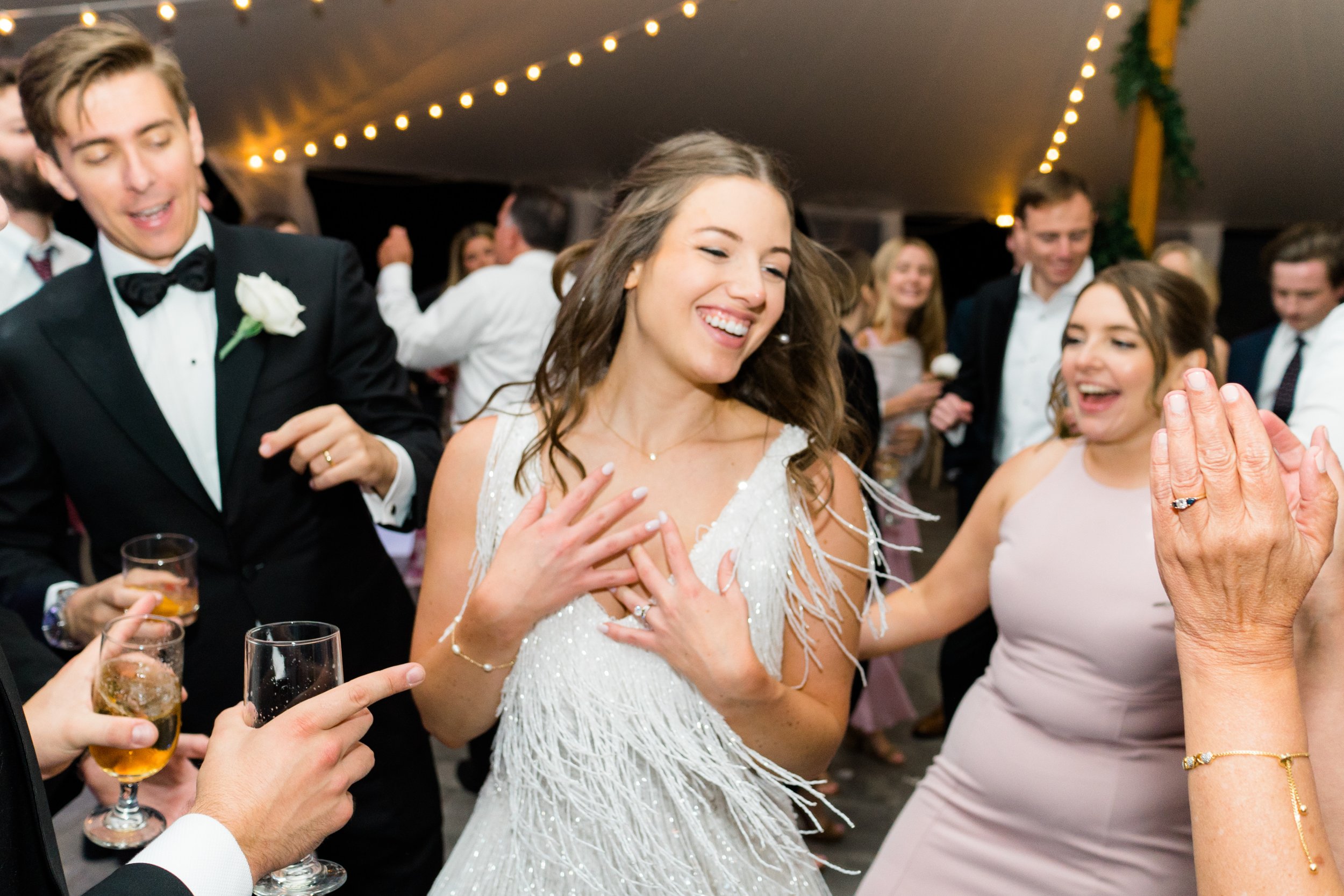 Candid dance floor photo of bride holding her heart and smiling while beaded dress flows behind her.