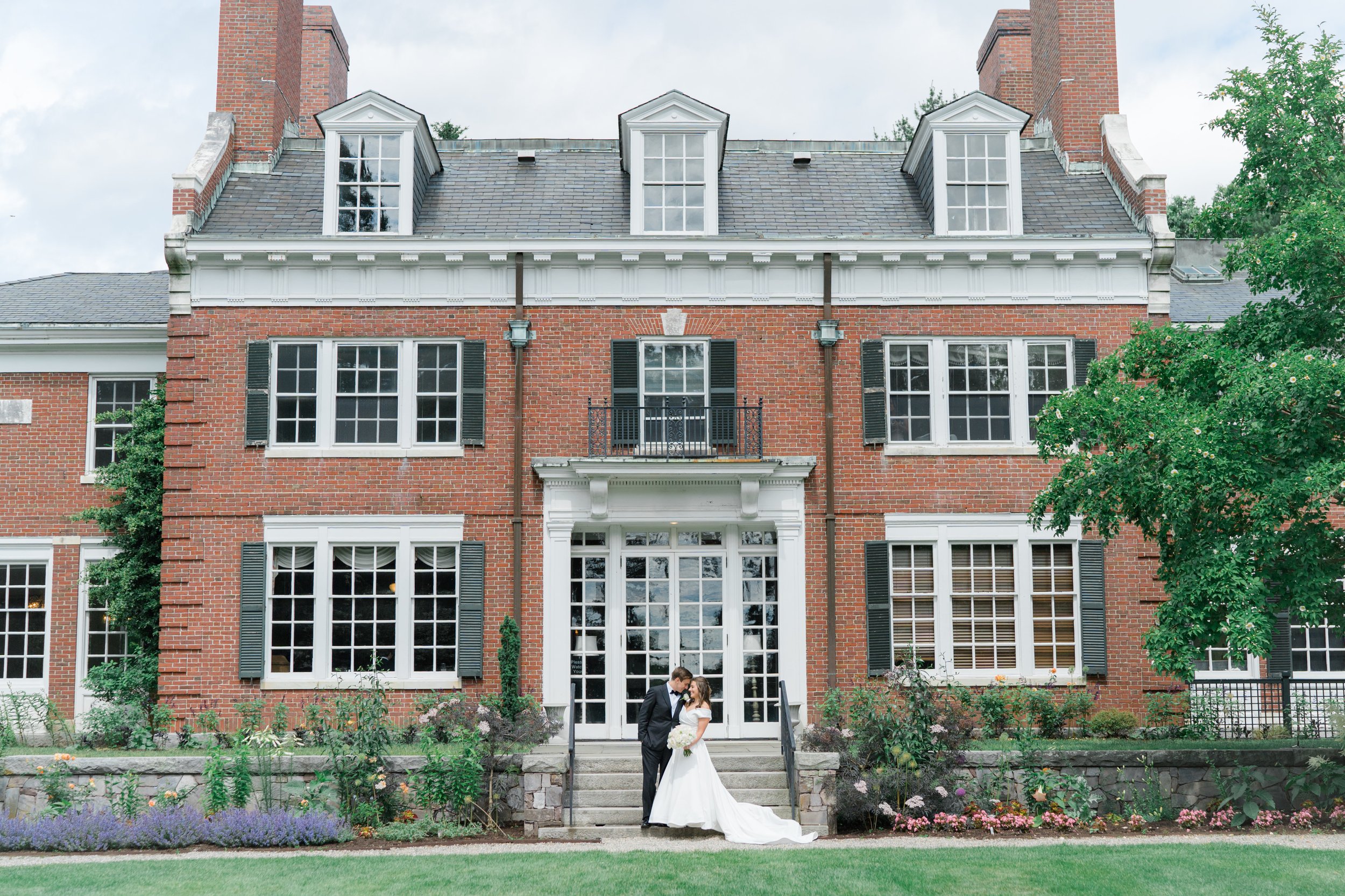 Bride and groom snuggle in front of the grand facade of the Bradley Estate. Boston Summer Wedding