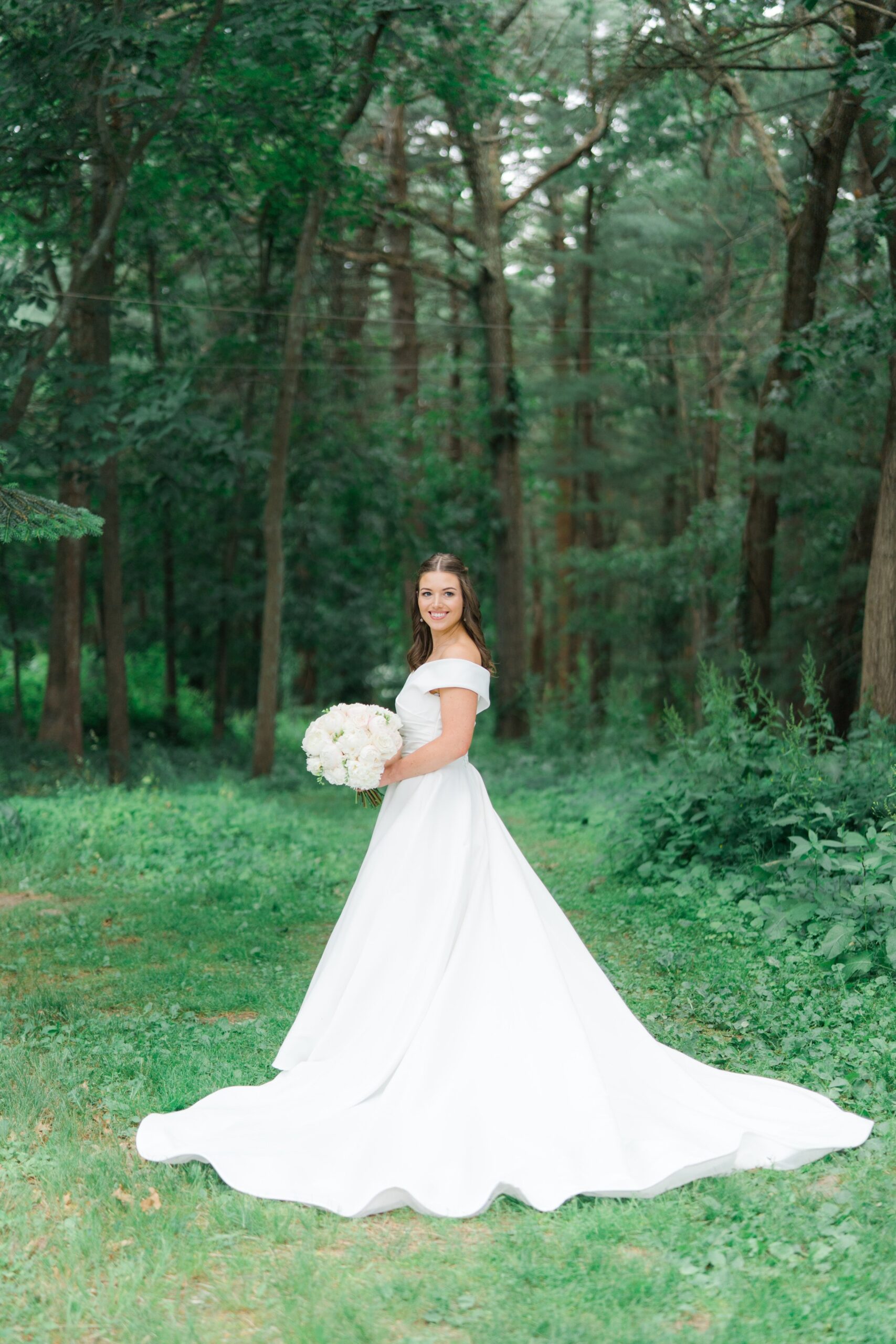 Wedding day bridal portrait in lush greenery on the grounds of the Bradley Estate. Off the shoulder wedding dress with long flowing train.