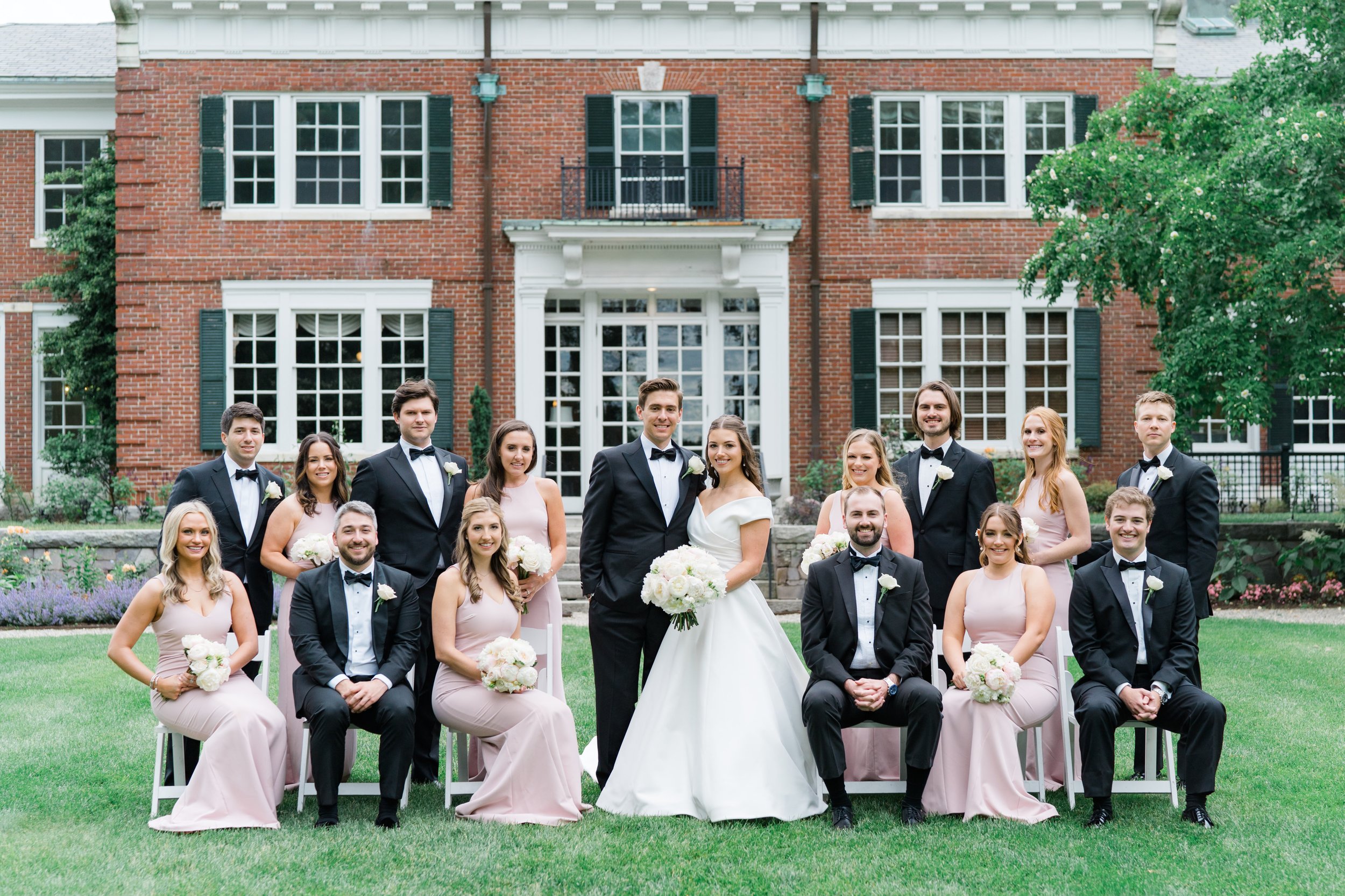 Full bridal party group picture on the lawn at the Bradley Estate. Black tie groomsmen and bridesmaids in dusty pink maxi dresses. Boston Wedding Photographer