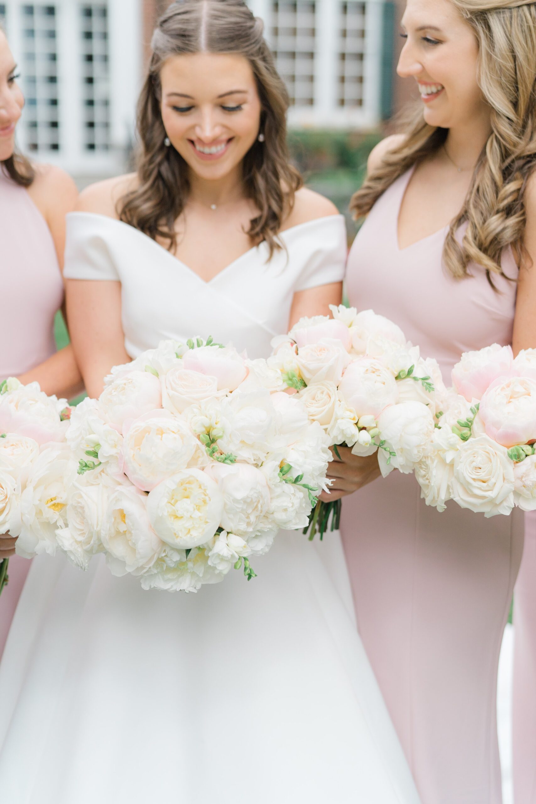 Bride and bridesmaids get close and look down at lush bouquets with a touch of pink.