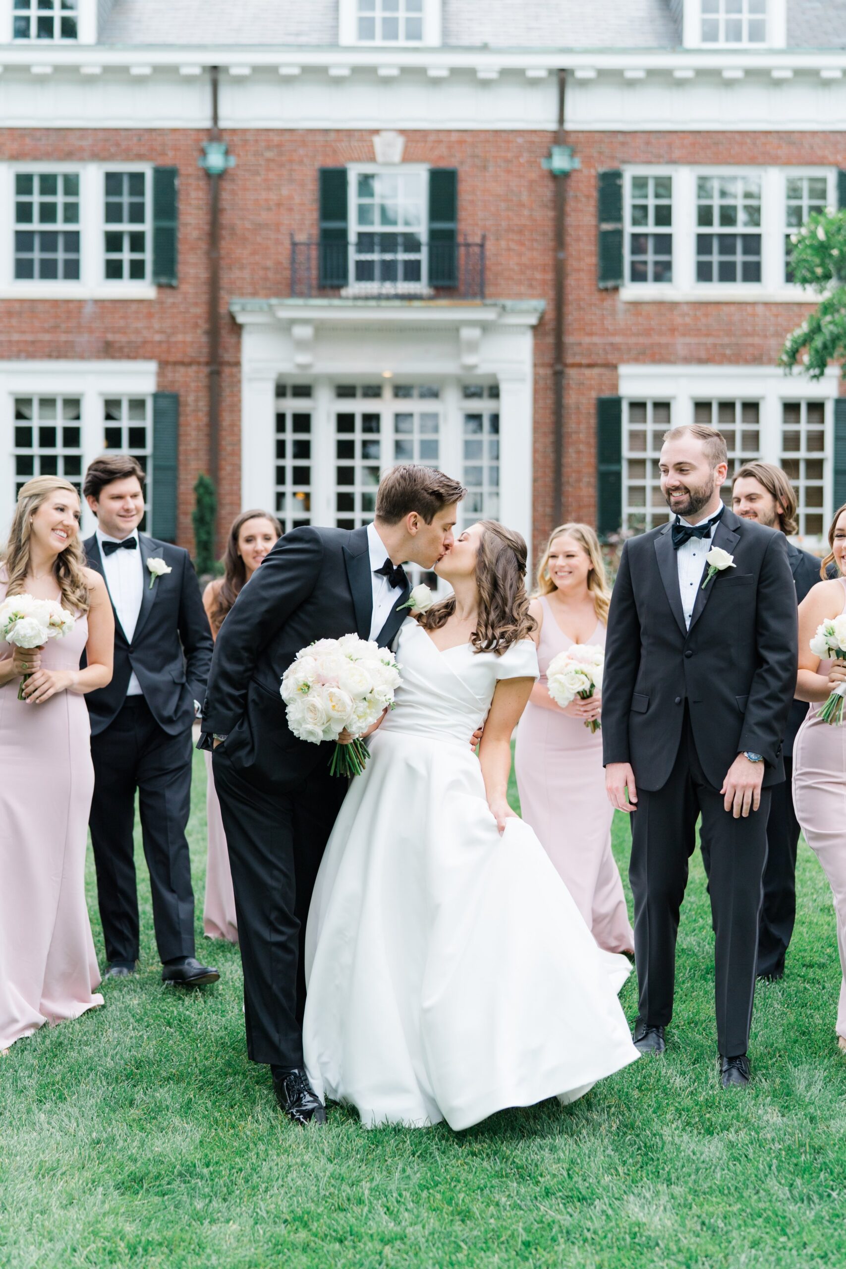 Groom grabs bride for dip kiss while walking with bridal party at boston summer wedding.