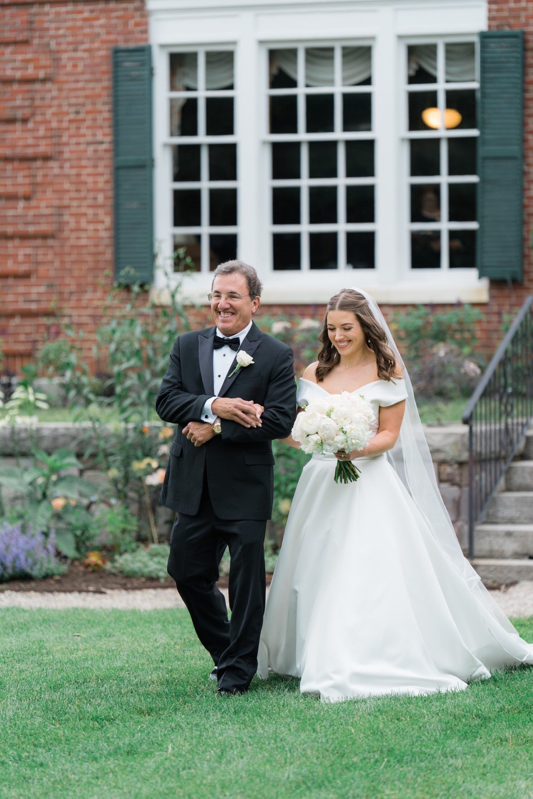 Father of the bride holds his daughters hand as they share a happy moment walking to boston summer wedding ceremony.