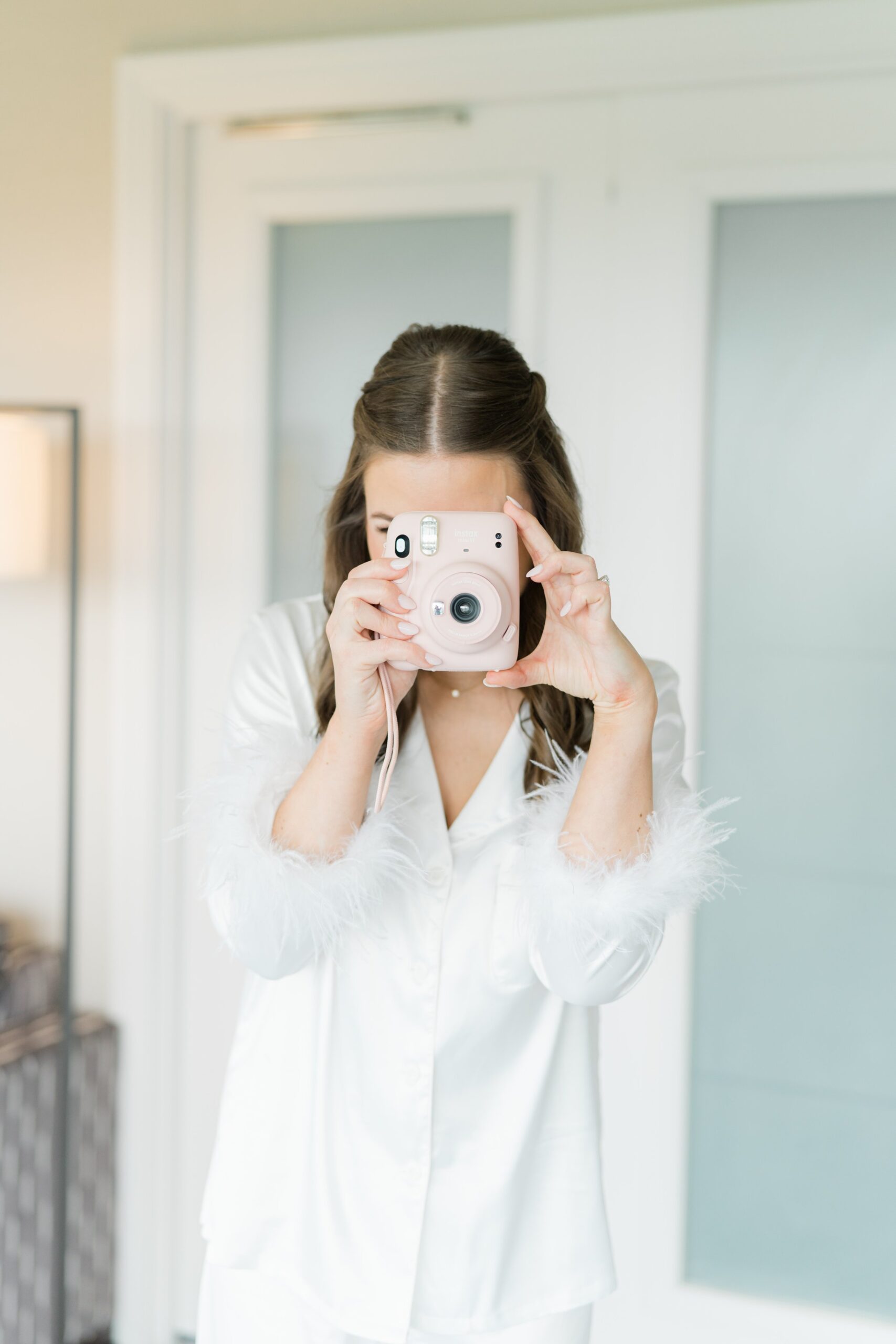fun picture of bride in feather sleeved pajamas holding pink polaroid camera
