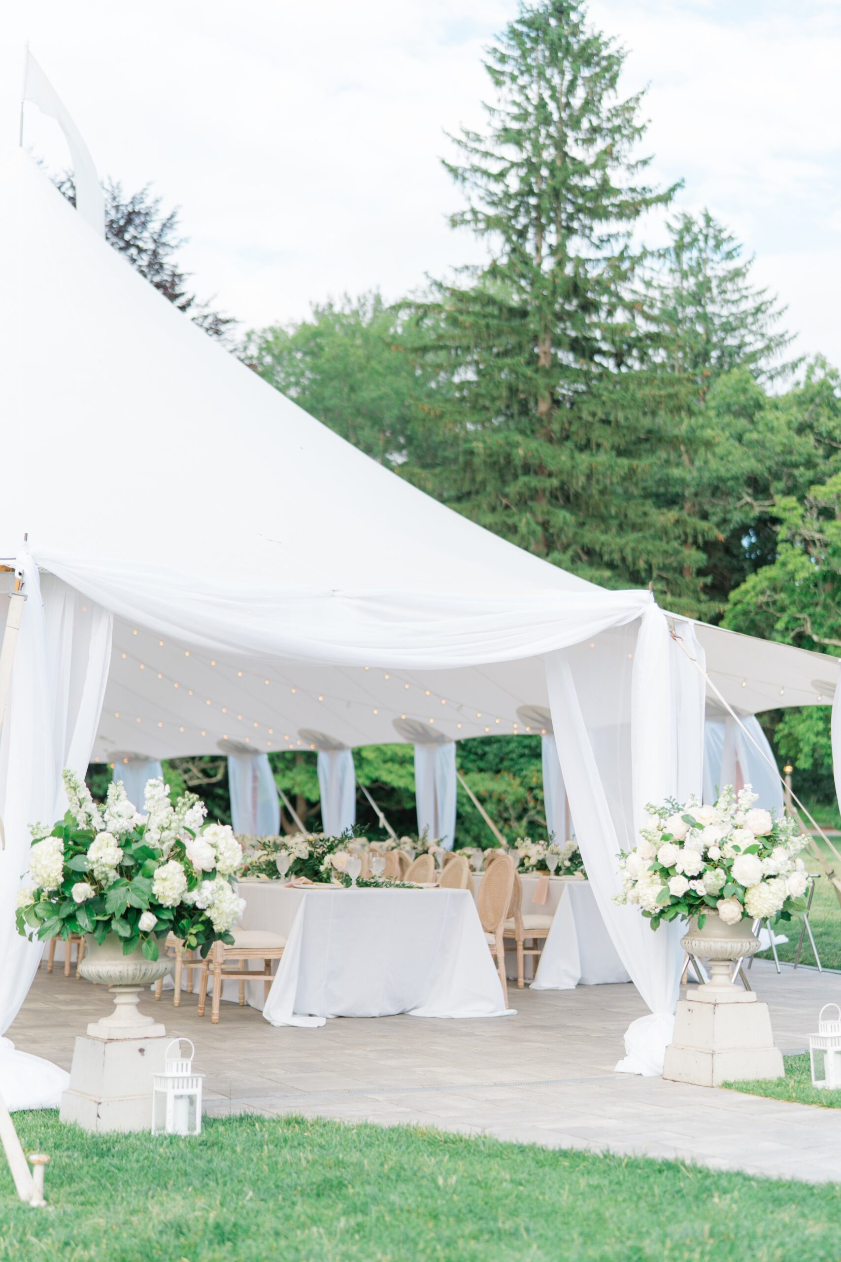 sperry tent with accents of white draping and pedestal flowers at tent entrance.