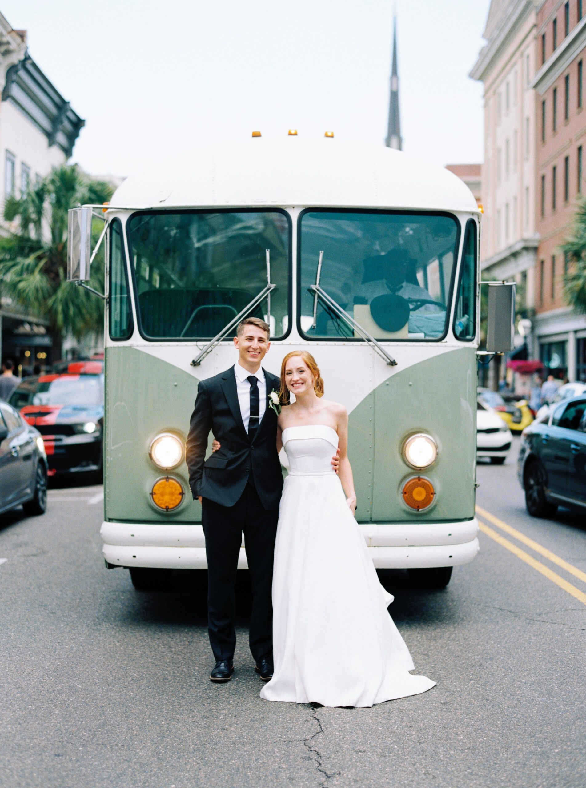 bride and groom stand in front of vintage bus on king street in downtown Charleston.