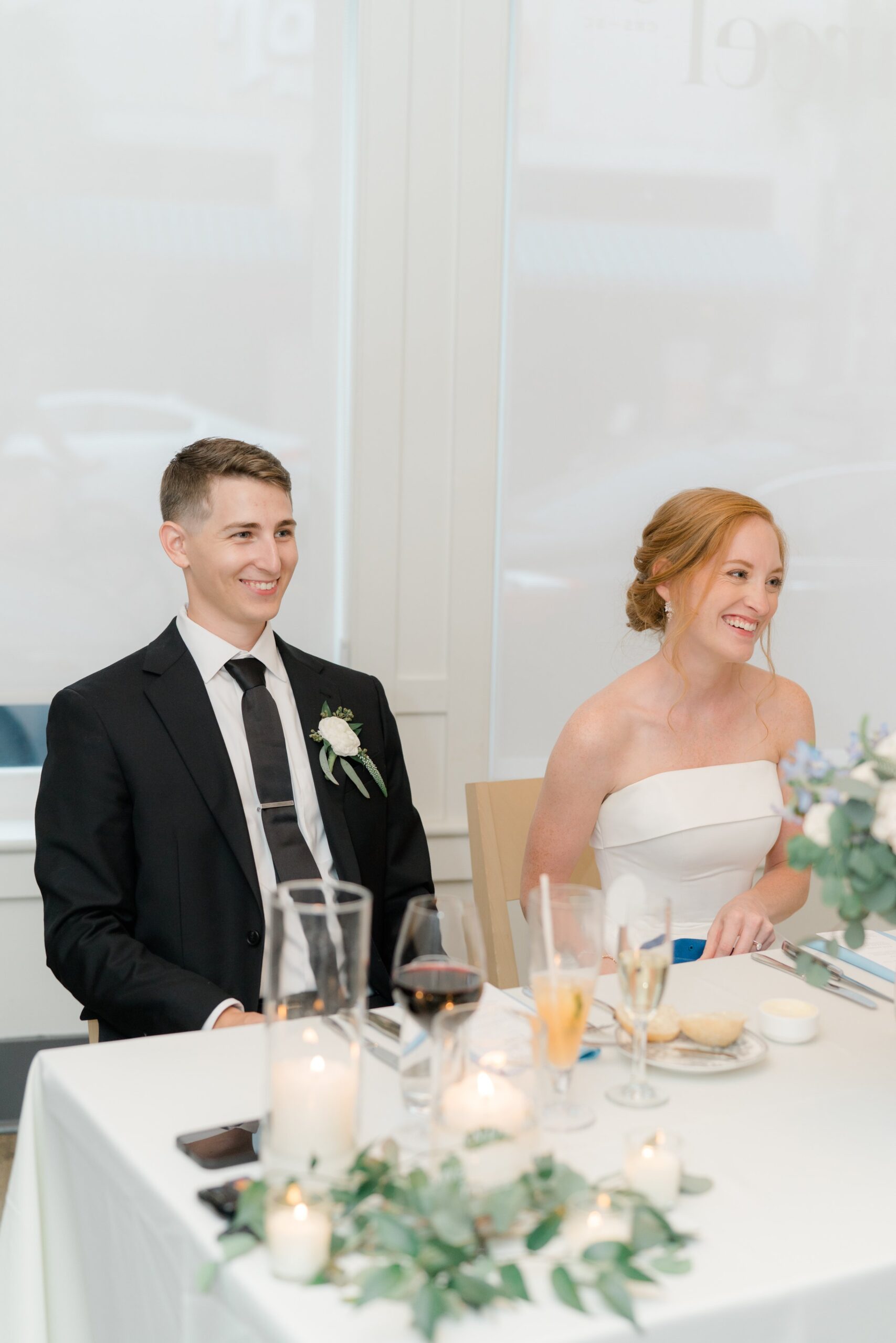 bride and groom enjoy speech from father of the bride at sweetheart table.