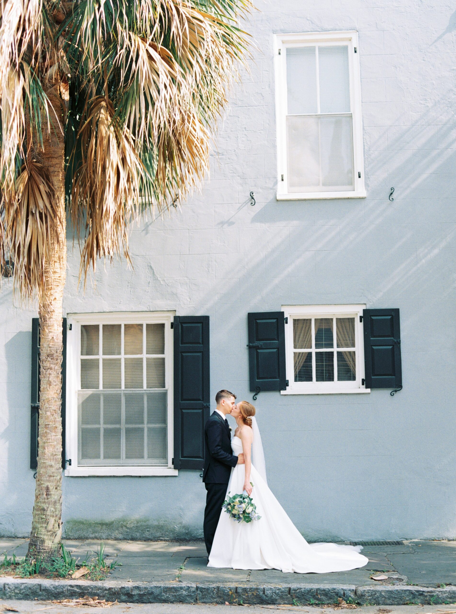 Downtown charleston film photography. Bride and groom with blue wall and palm tree with golden light