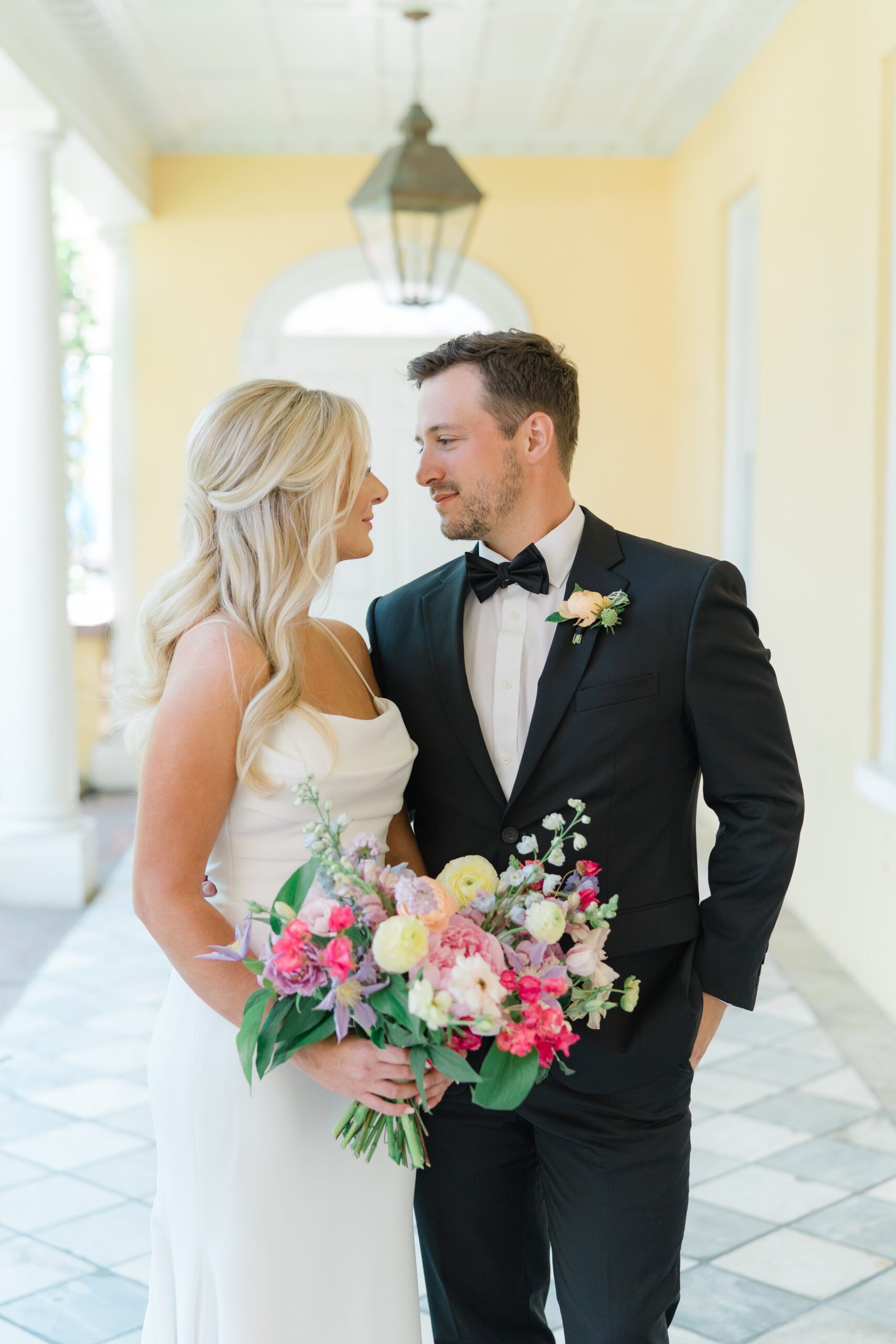 spring florals bride and groom standing under portico at william aiken house in downtown charleston. black tie groom