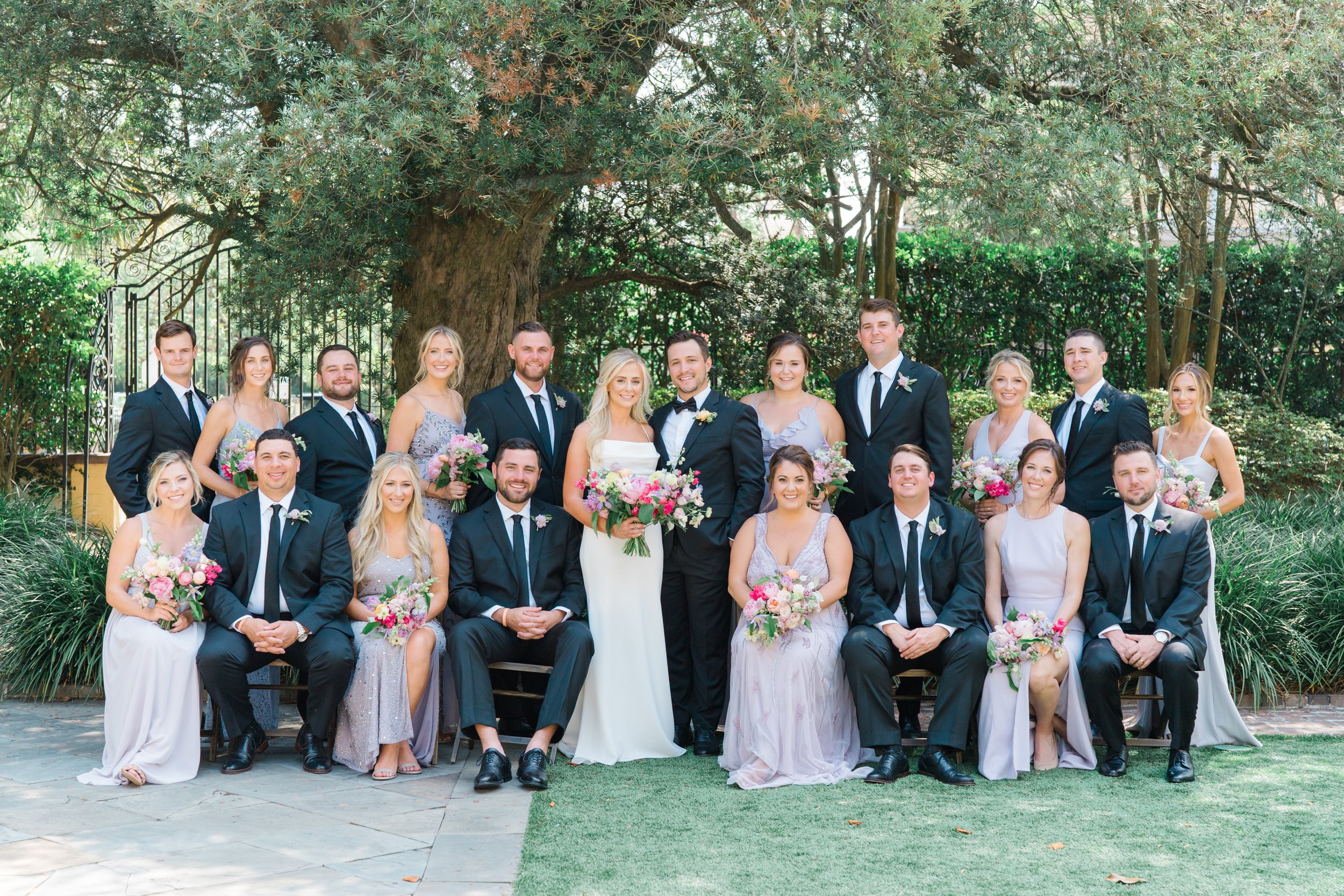 full bridal party posed photo with half of group sitting at william aiken house. Mixmatched bridesmaids dresses. Charleston wedding photographer.