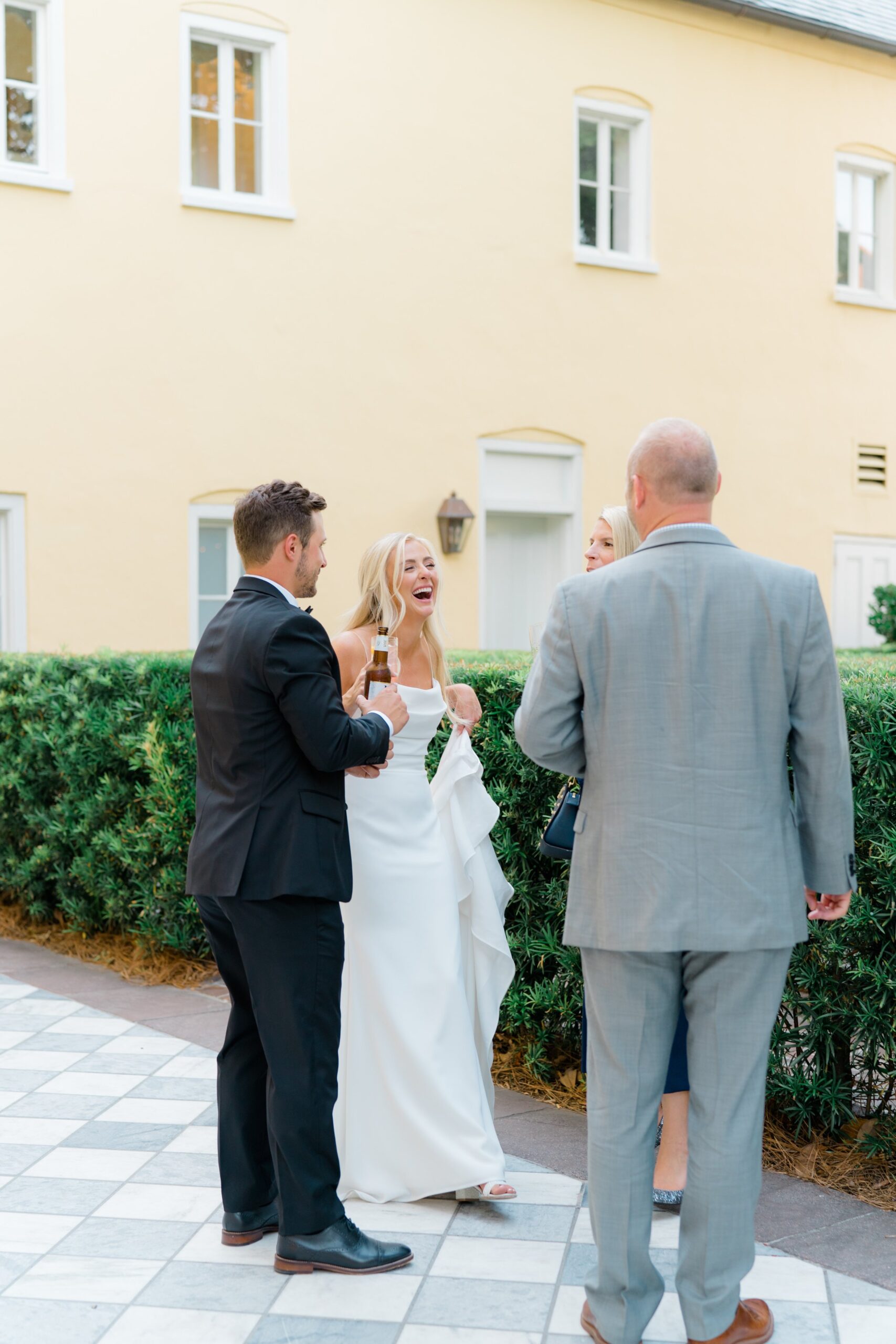 bride and groom laugh with wedding guest with yellow wall and checkerboard floor