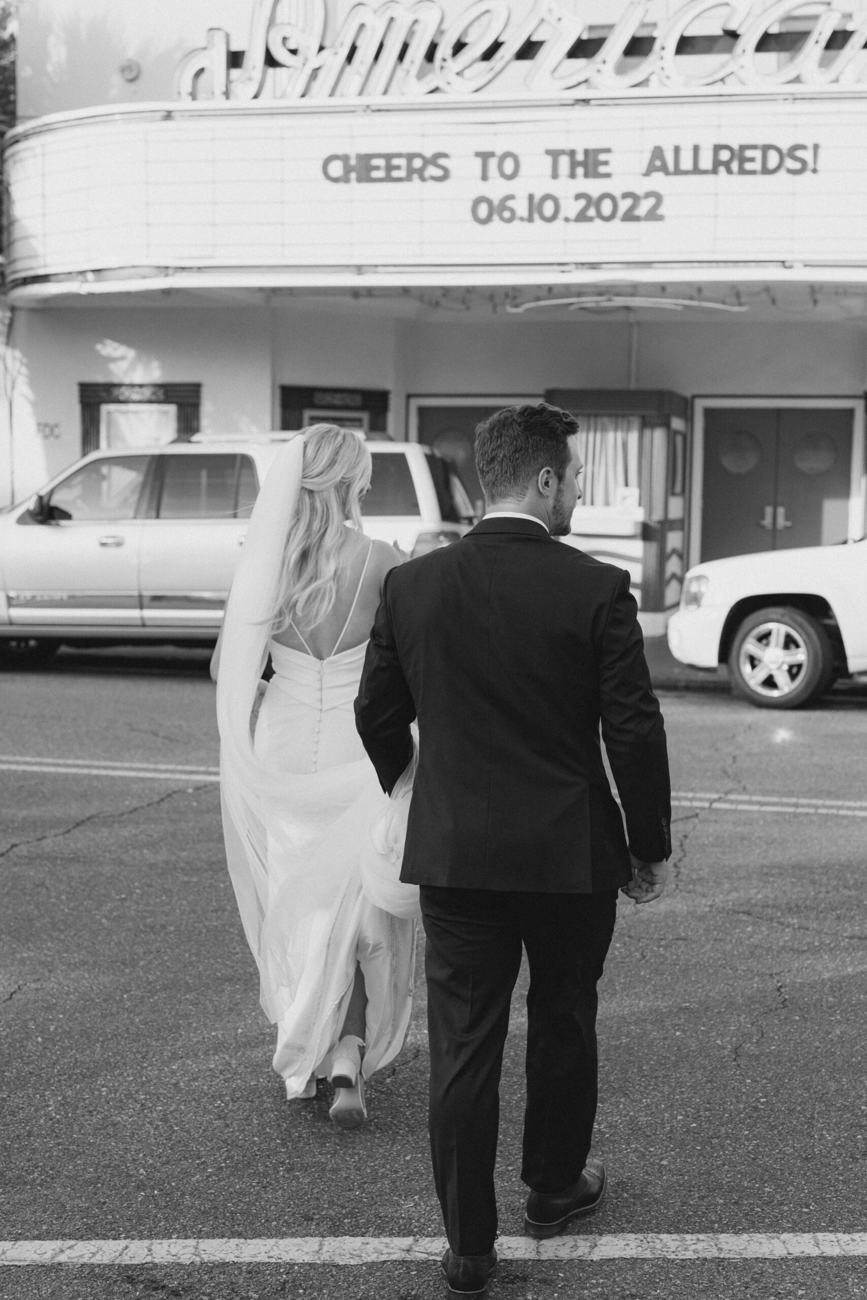 black and white photo of bride and groom crossing king street with movie theater marquee