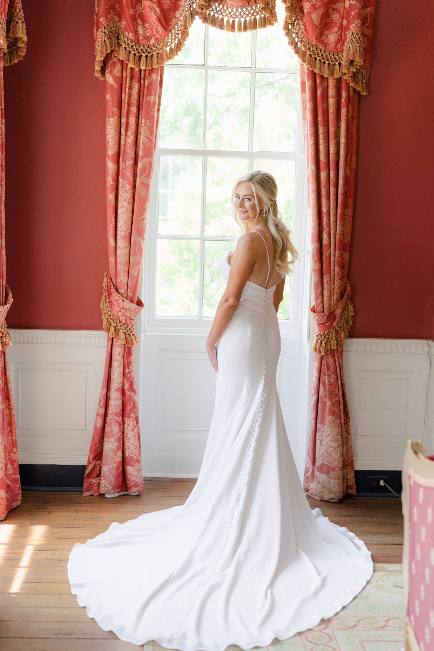 spaghetti strap wedding dress bride standing in front of window in historic red room at wedding venue in downtown Charleston