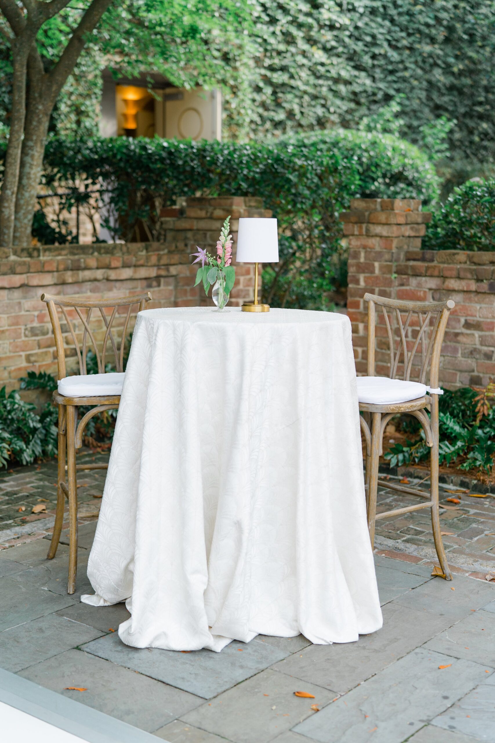 classy high cocktail table with textured tablecloth and small lamp.