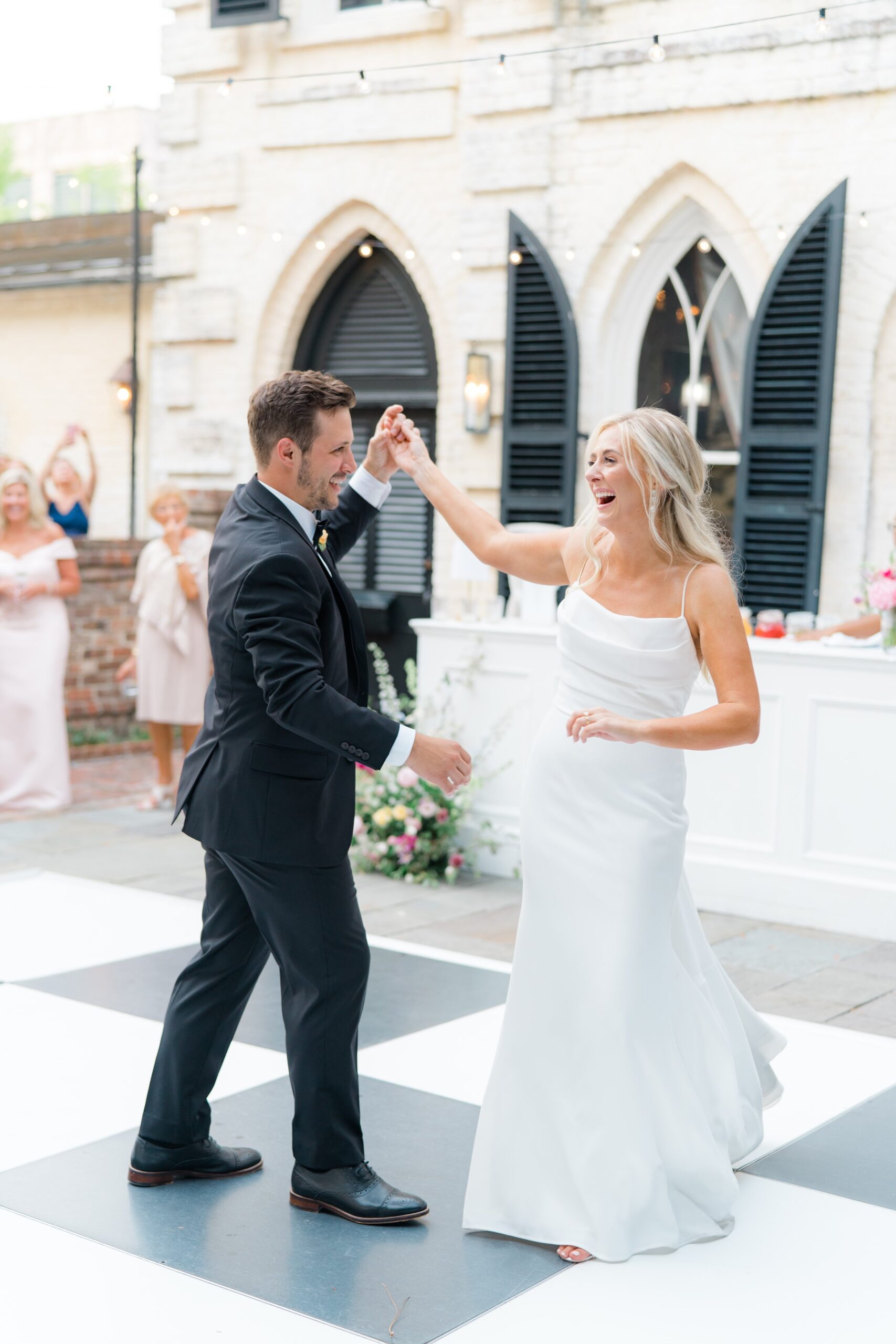 bride laughs through spin move during first dance on black and white checkerboard dance floor