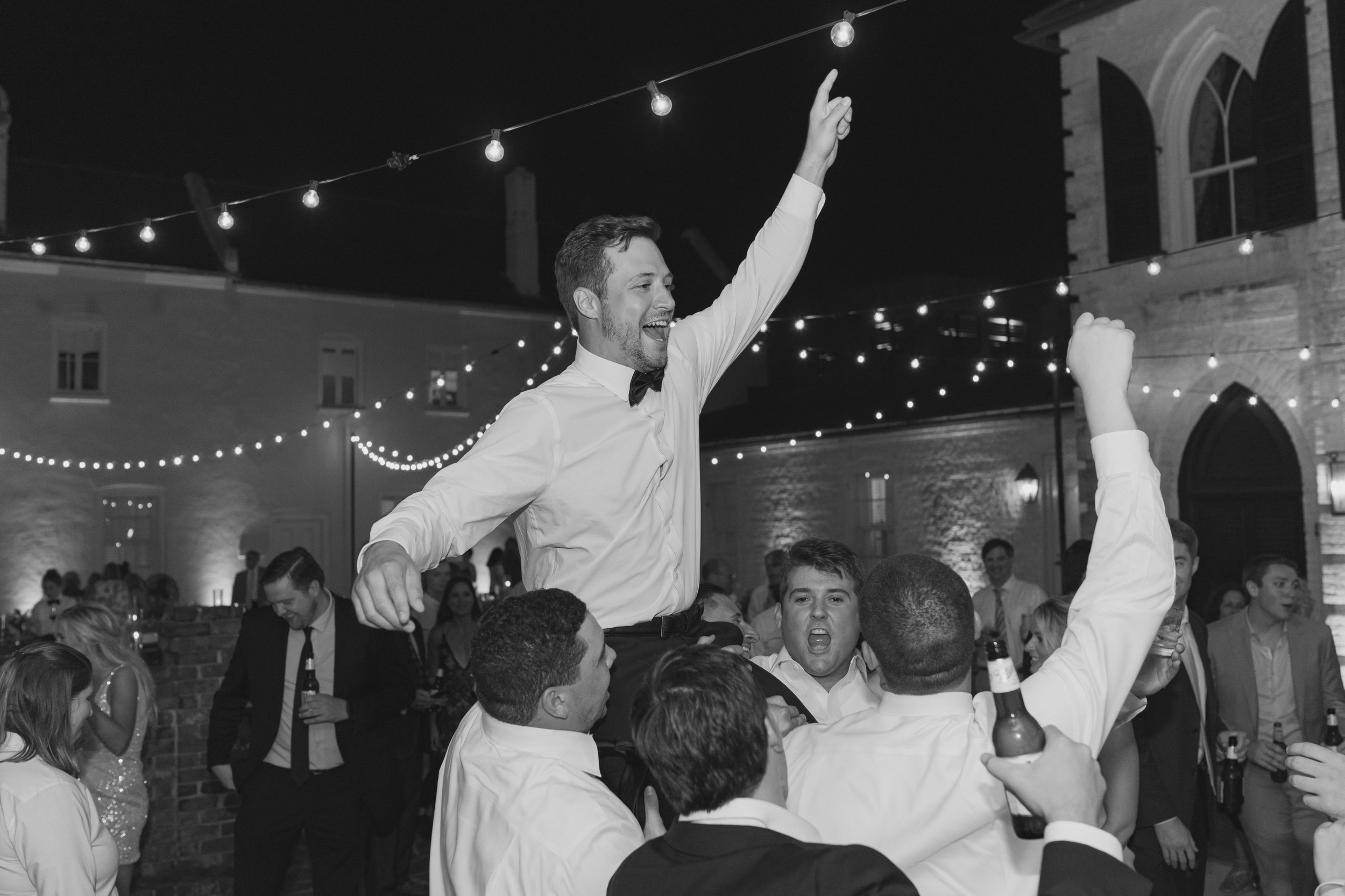 groom gets picked up in celebration during outdoor dance party at wedding reception.