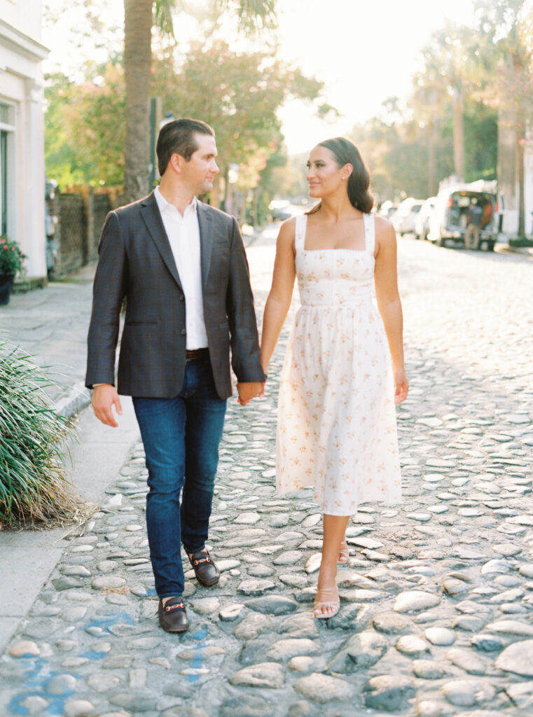 Engagement session with couple walking on cobblestone street in historic Charleston. Golden sunshine film photos.