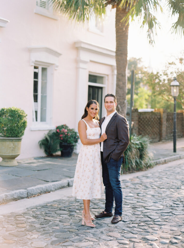 Film engagement photos with cobblestone, palm tree, and Charleston historic pink house.