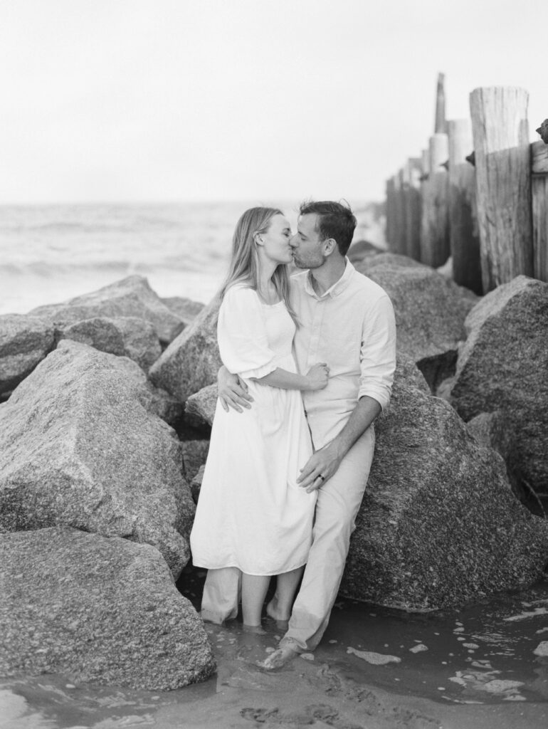 Engagement photos with couple kissing on rocks at the beach. 